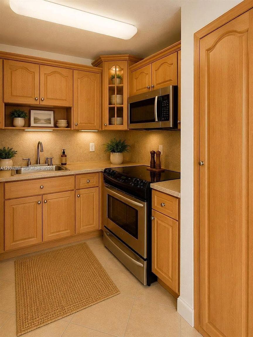 Kitchen featuring wood cabinetry with glass-front display accents, stone-composite countertops, integrated under-cabinet lighting, stainless steel appliances, and a full-height pantry closet