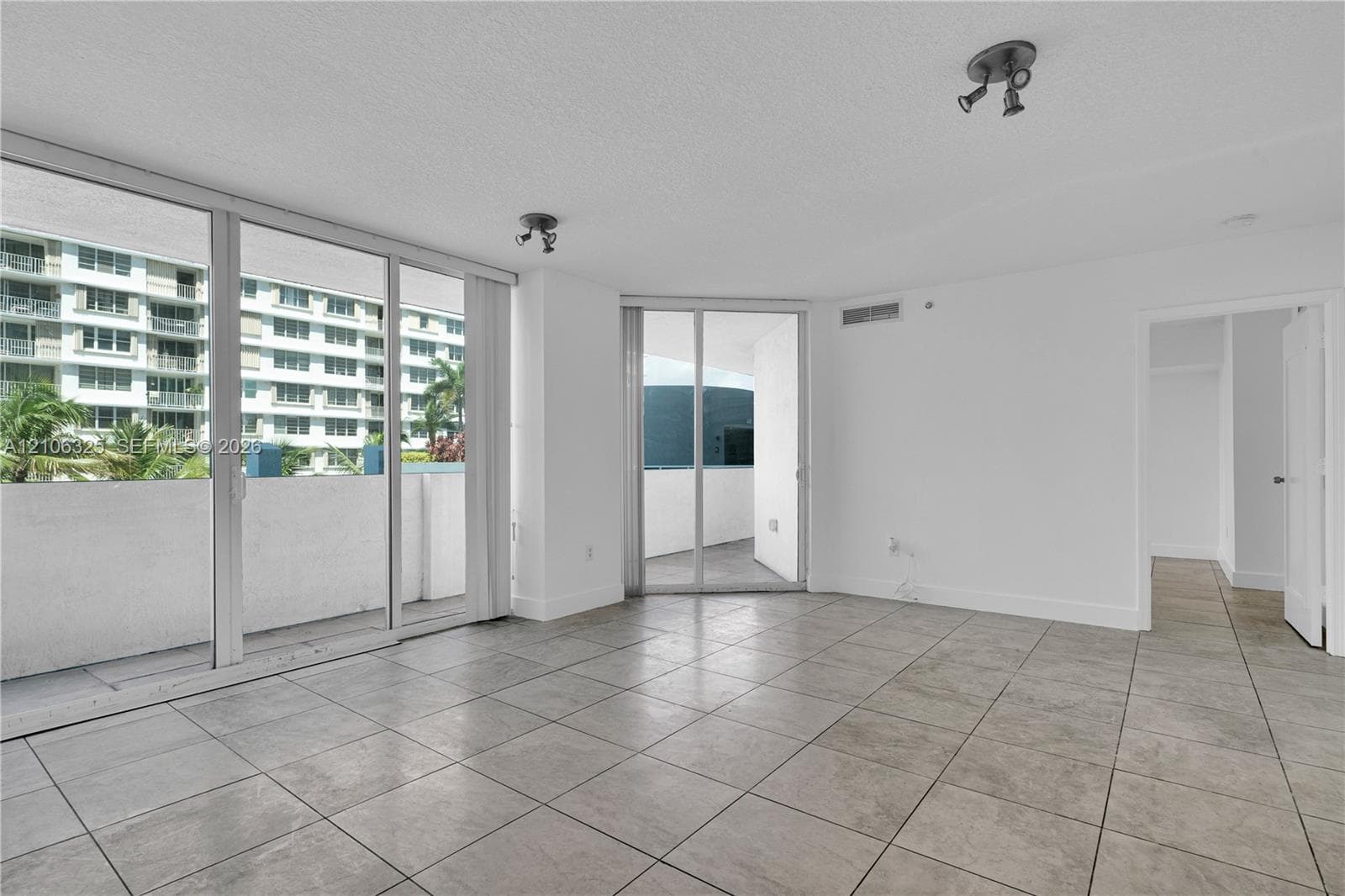 Open floor plan featuring oversized tile flooring, floor-to-ceiling glass sliding doors, dual-access balcony entries, and directional track lighting