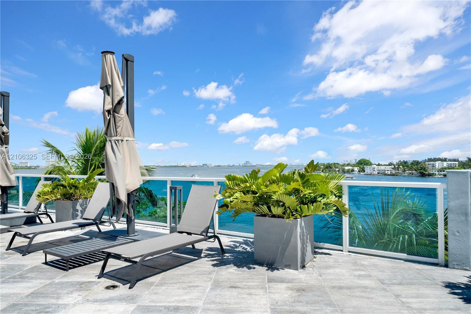 Expansive rooftop terrace featuring large-format stone tile flooring, a transparent glass railing, and integrated metal lighting fixtures