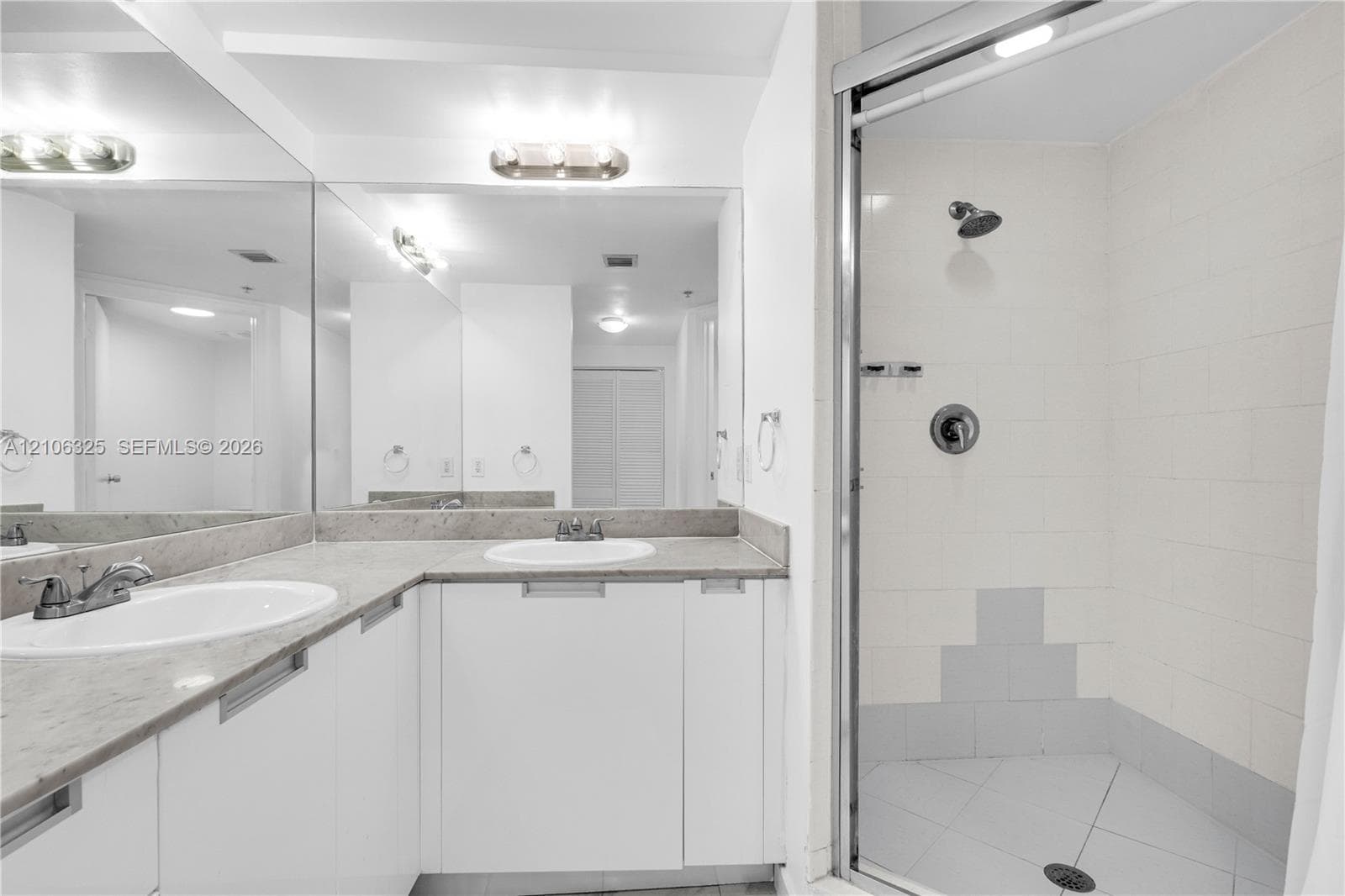 Dual-sink vanity with stone-finish countertop, full-width wall mirror, and walk-in shower with tiled surround