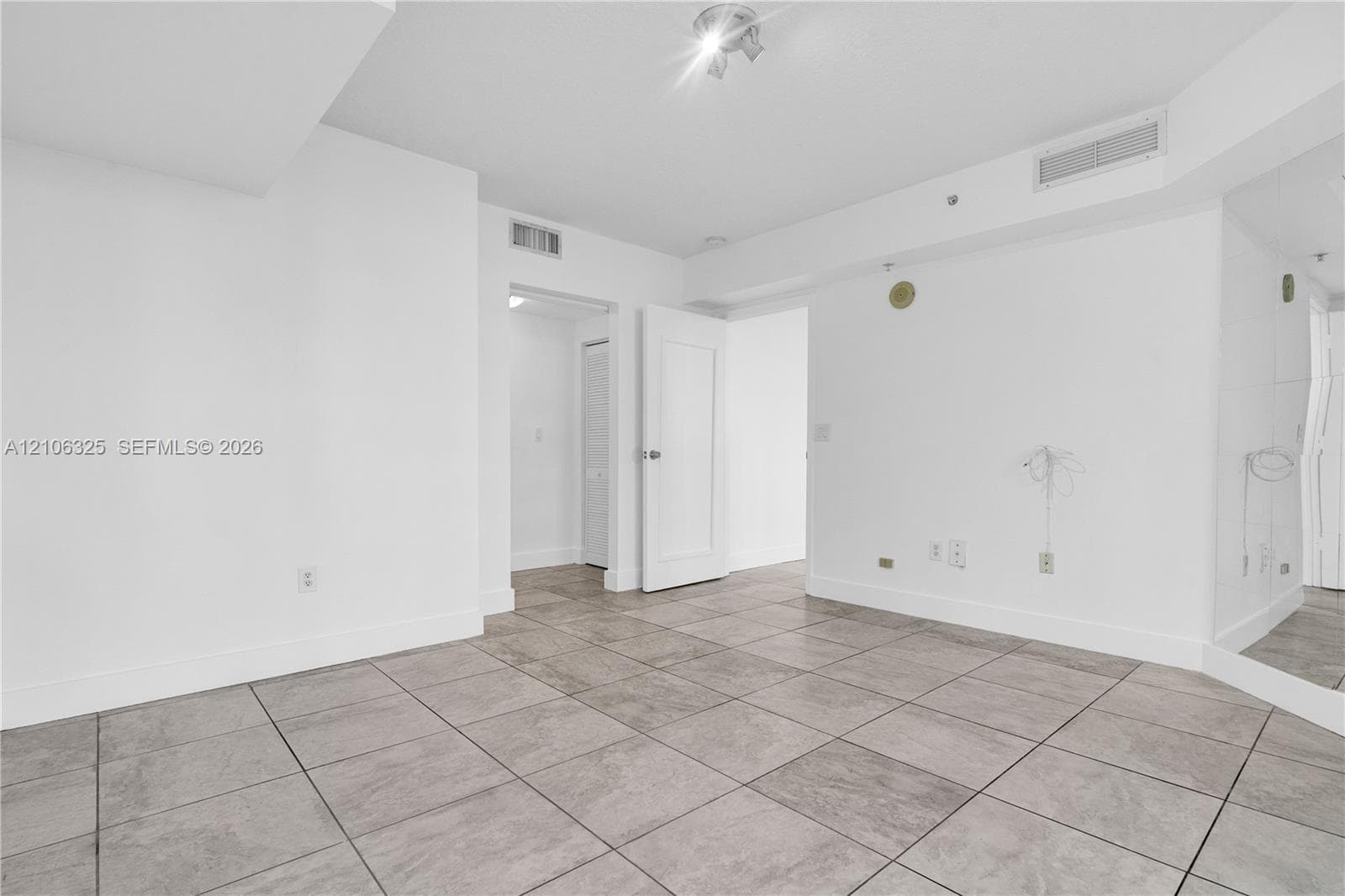Neutral-toned tile flooring, white interior finishes, mirrored wall paneling, and a flush-mount ceiling fixture