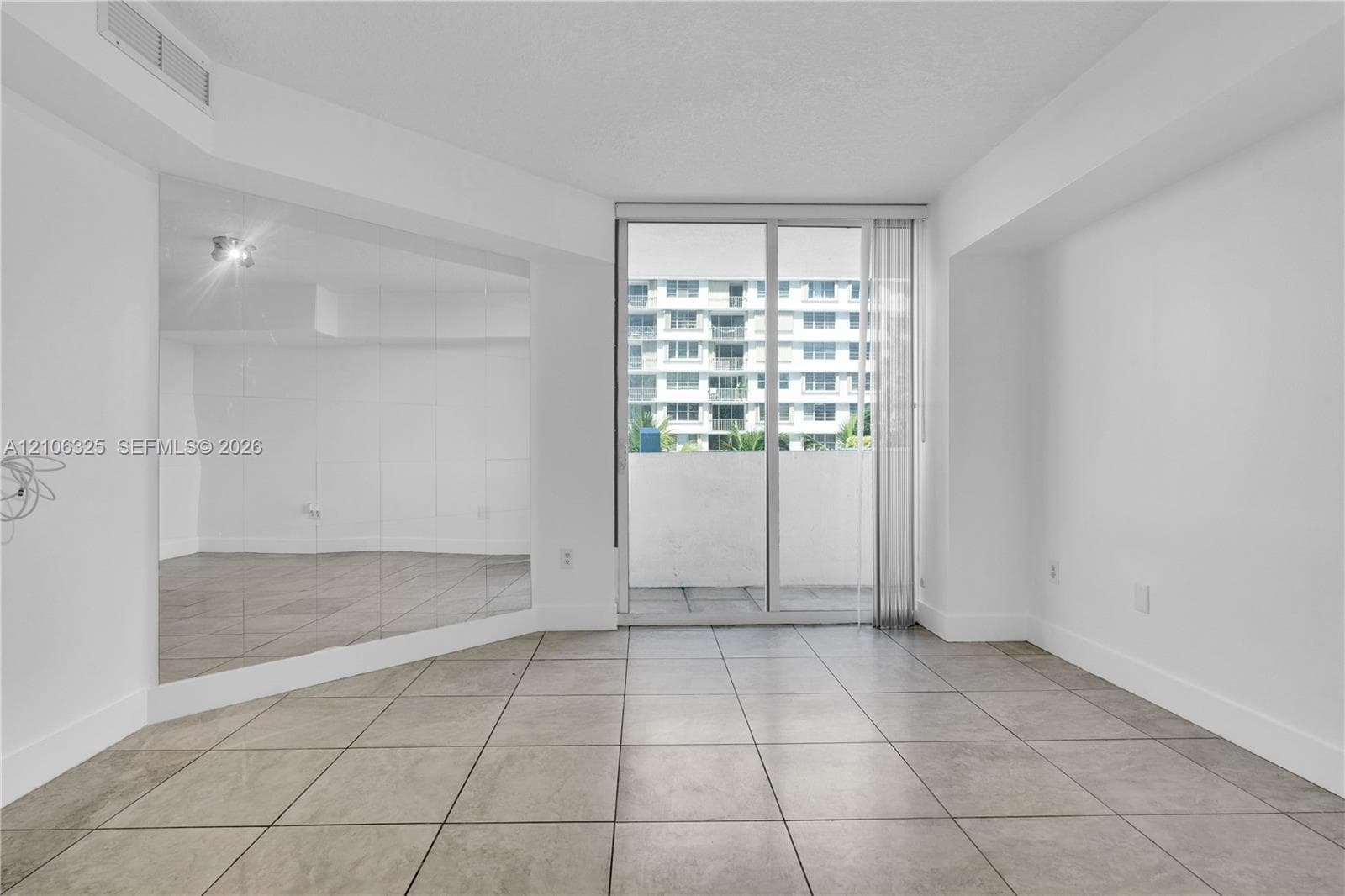 Living space featuring large-format ceramic tile flooring, a full-wall mirror, and sliding glass doors with access to a private balcony