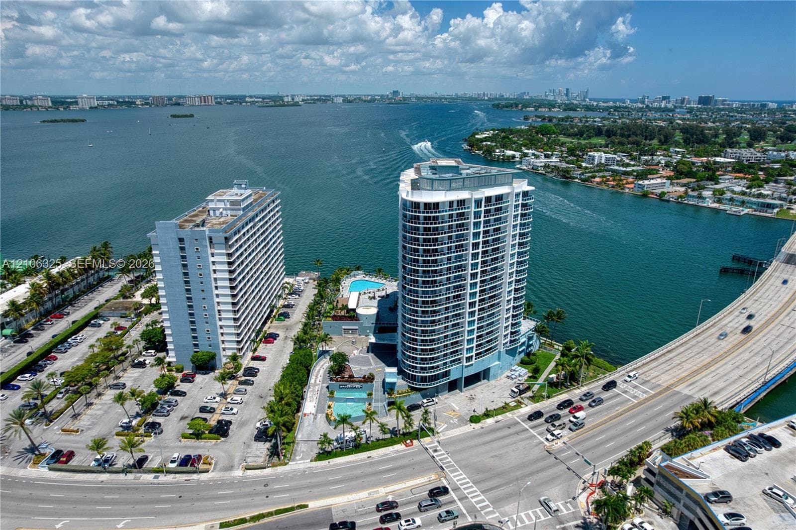 High-rise waterfront property featuring extensive glass-paneled balconies, a multi-level outdoor swimming pool, and paved surface parking