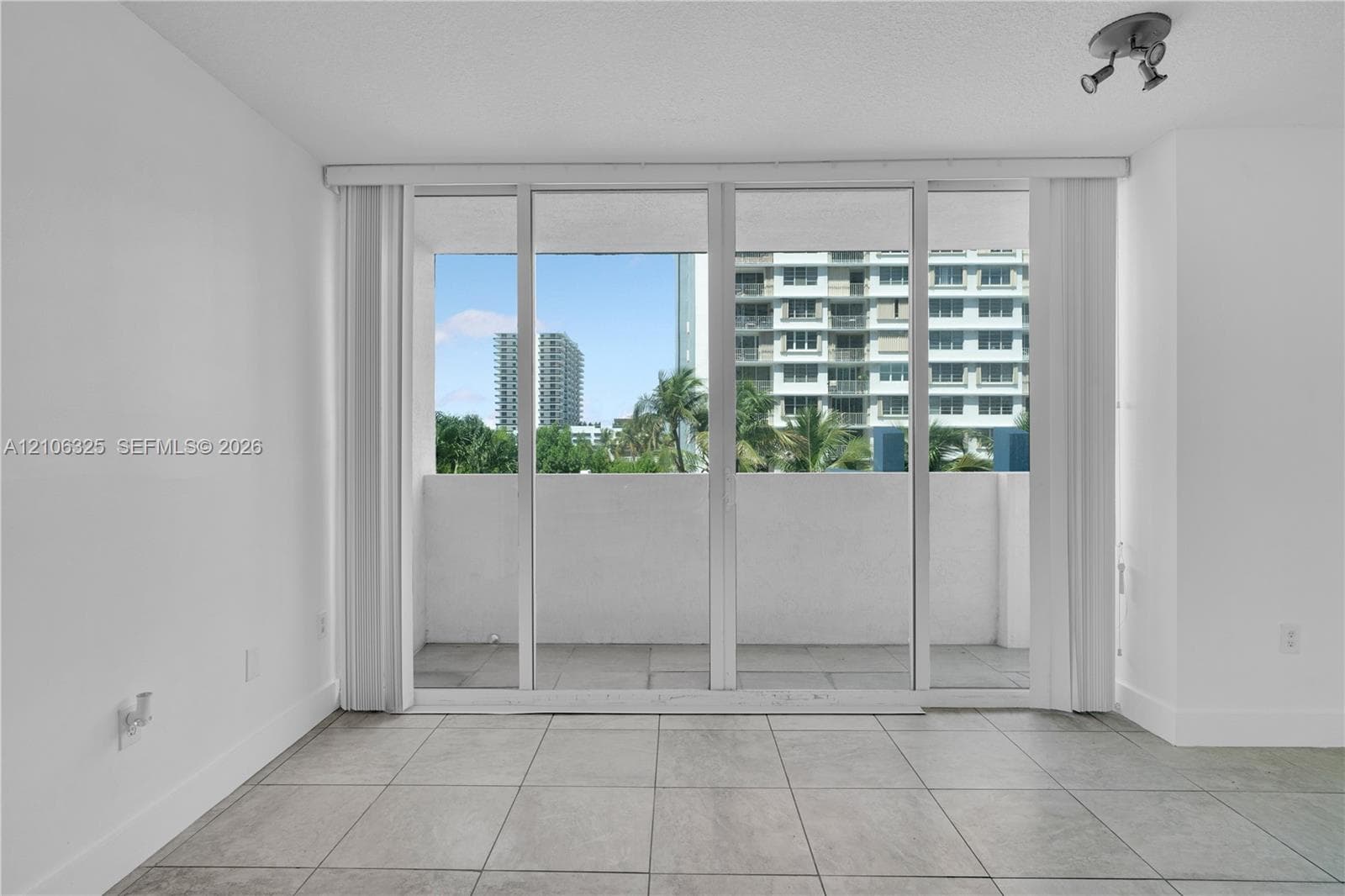 Floor-to-ceiling glass sliding doors, large-format tile flooring, and an attached balcony with concrete parapet