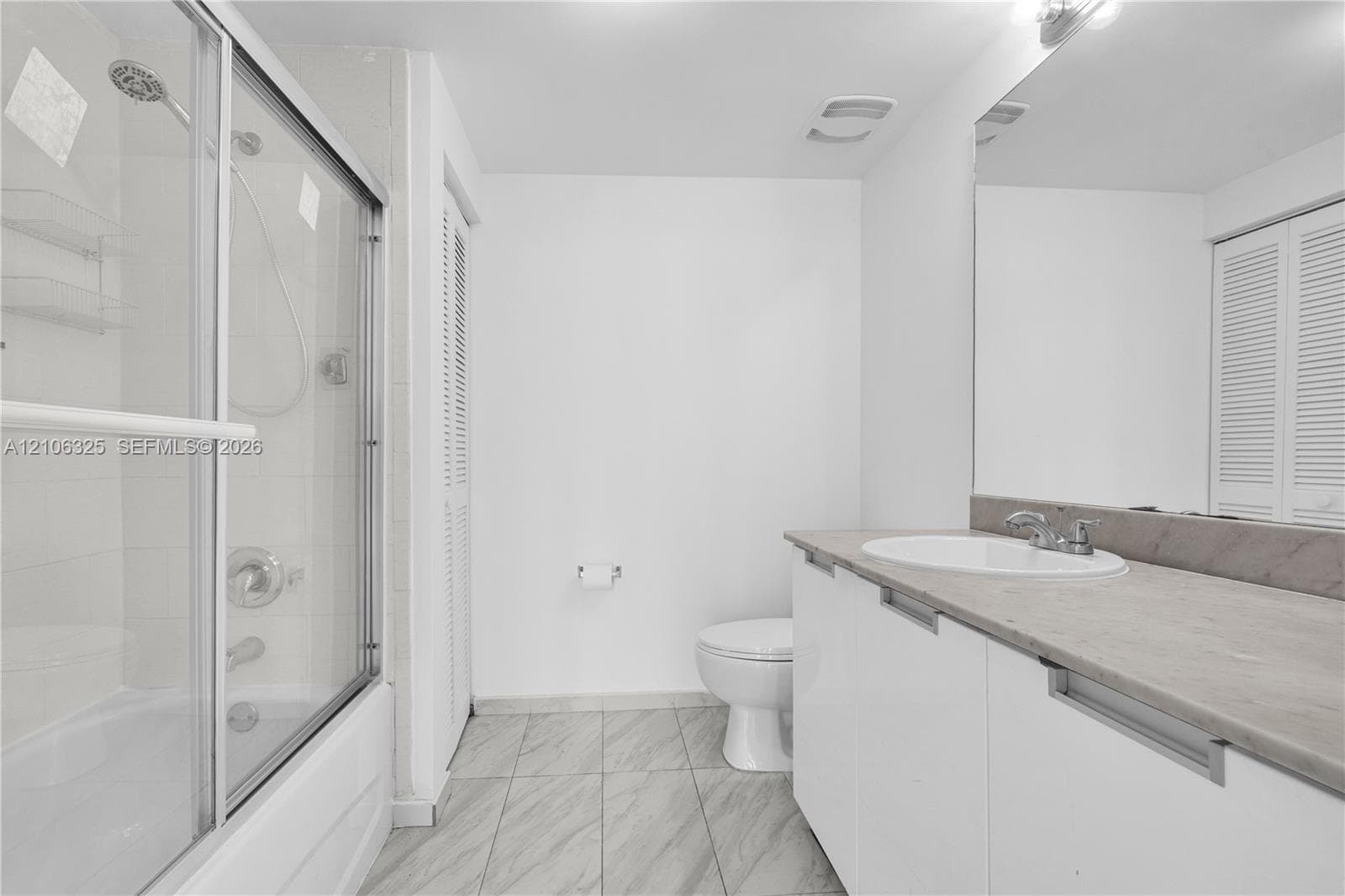 Full-length shower with glass enclosure, white vanity with stone-finish countertop, undermount sink, and tile flooring