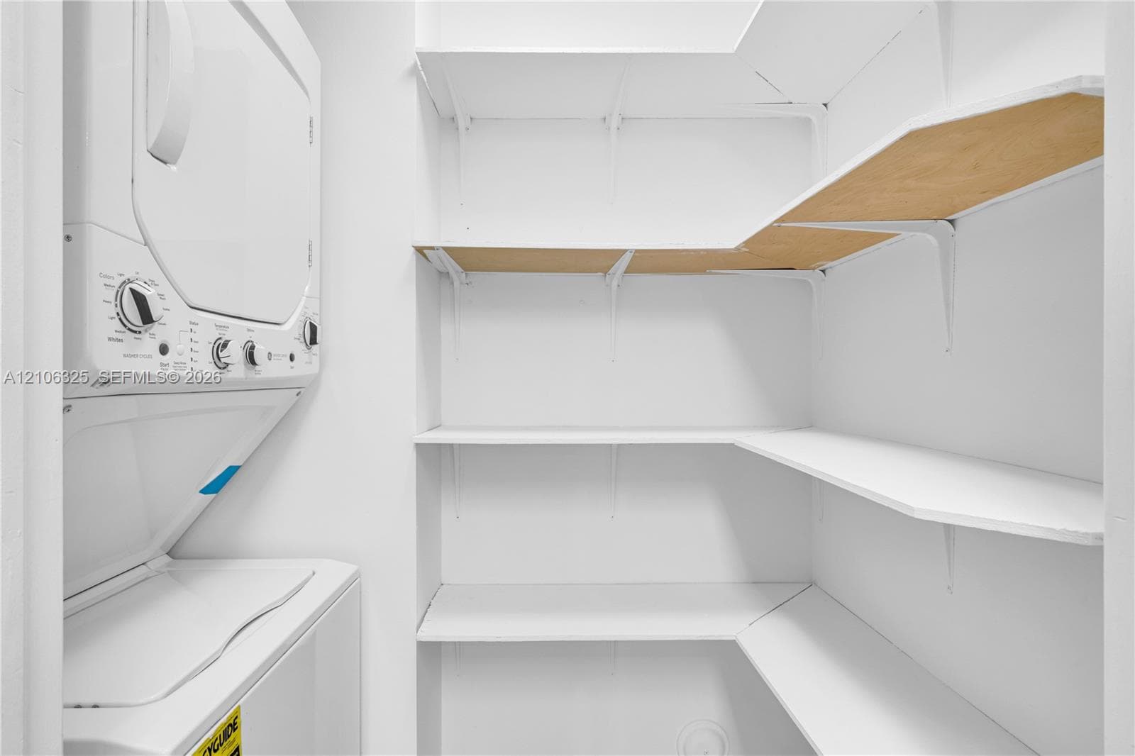 Stacked laundry unit featuring white finished appliances and tiered built-in shelving with bracket supports