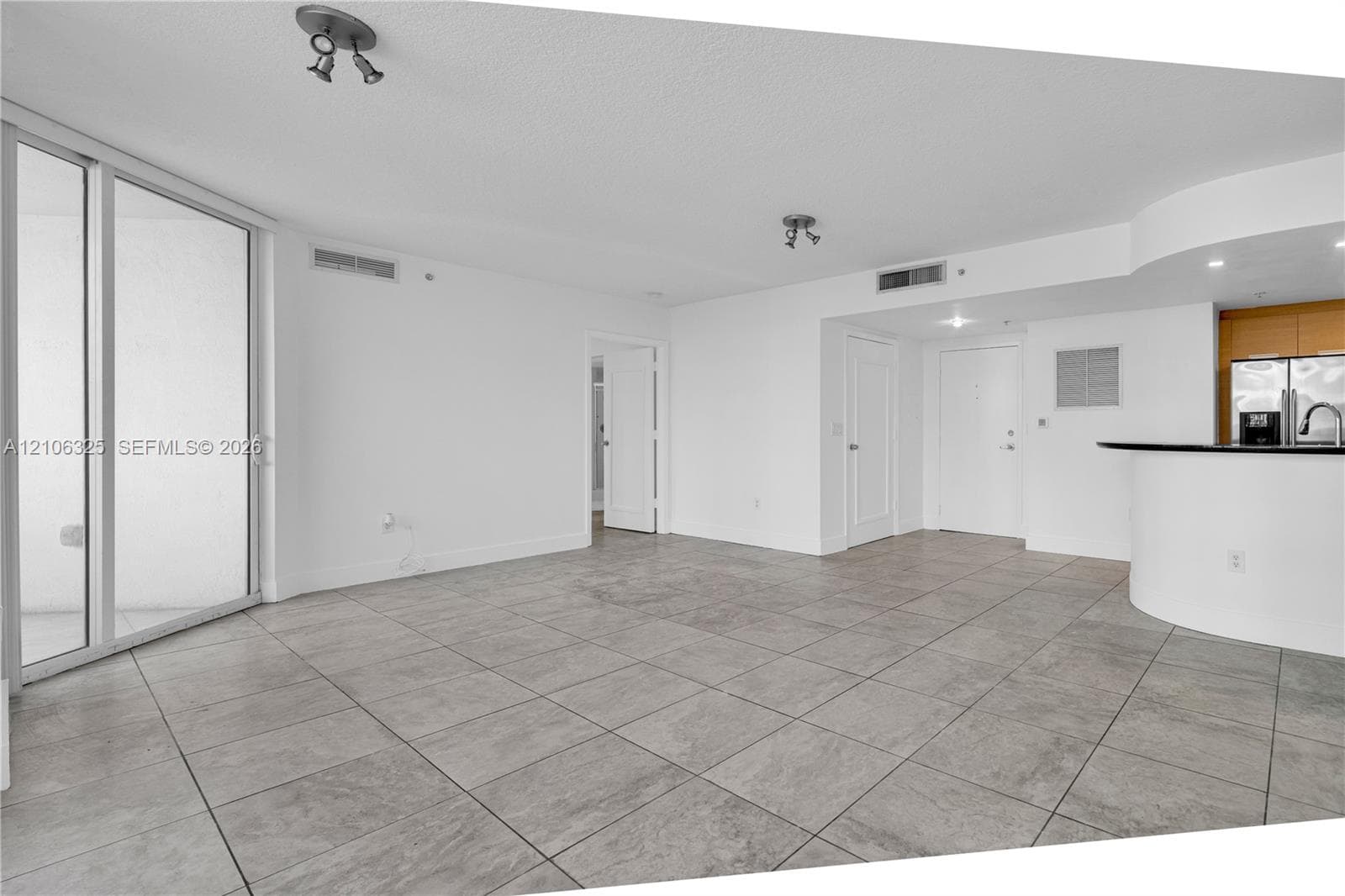 Open-concept area featuring oversized ceramic floor tile, a curved breakfast bar with a dark countertop, floor-to-ceiling sliding glass doors, and dual-track ceiling lighting