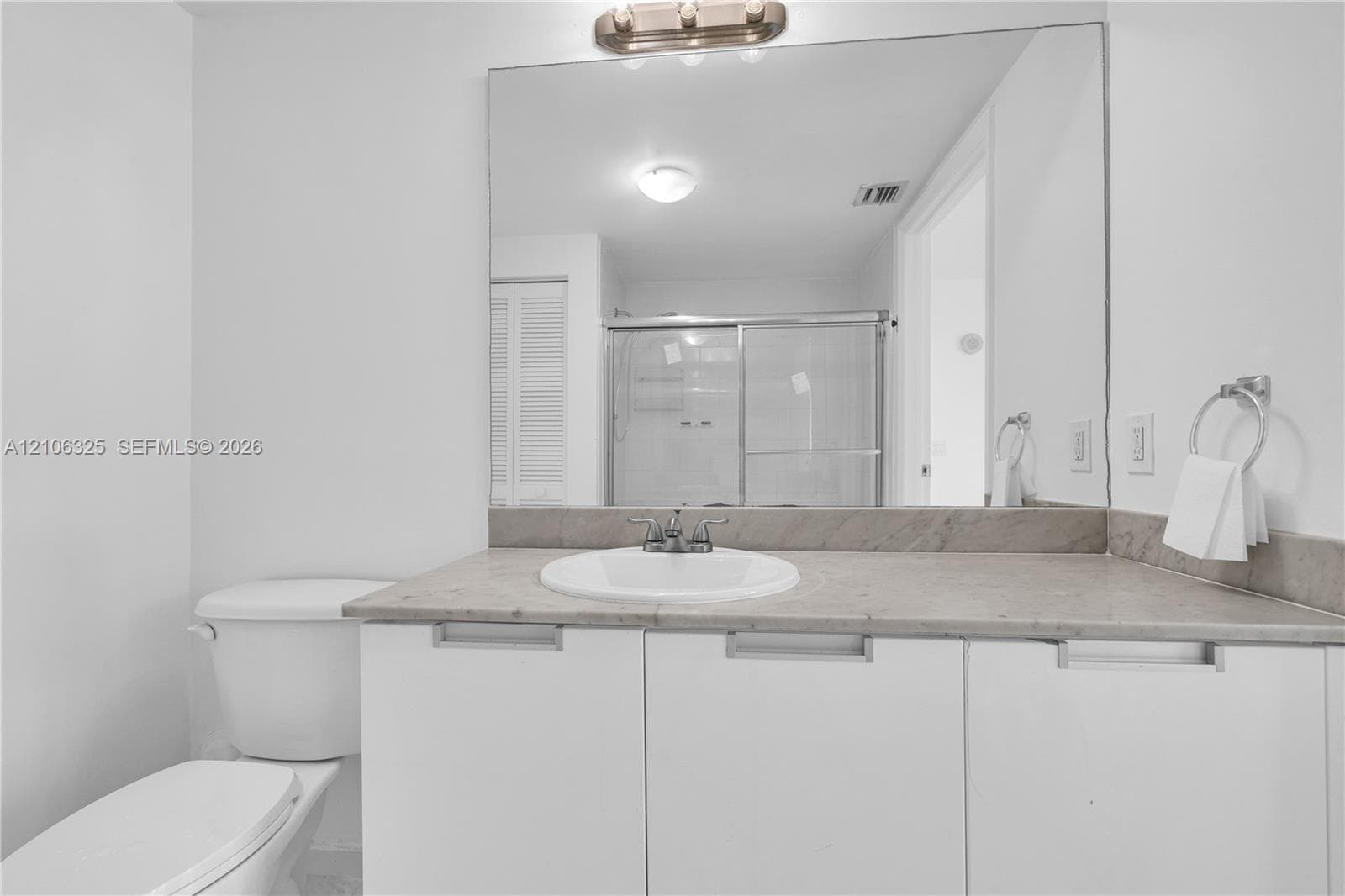 Bathroom featuring a vanity with a stone countertop, integrated sink, and polished chrome hardware, complemented by a full-width wall mirror and three-light overhead fixture