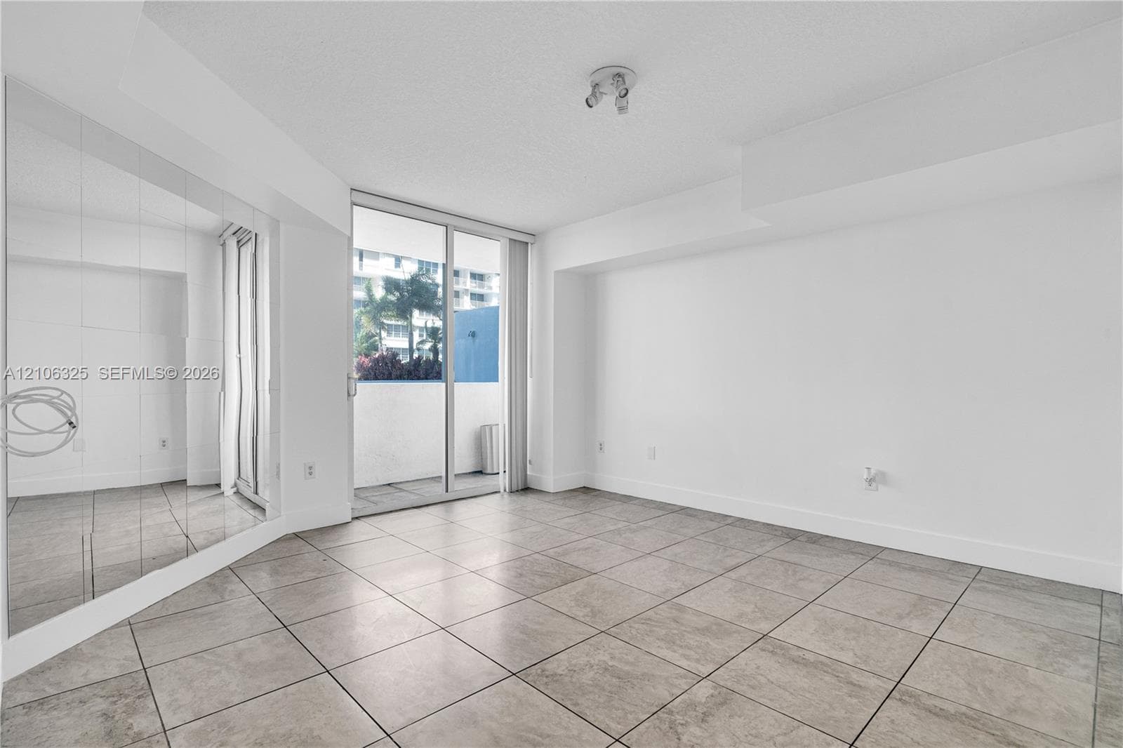 Neutral-toned tile flooring, floor-to-ceiling wall-mounted mirror, and sliding glass doors with access to an exterior balcony