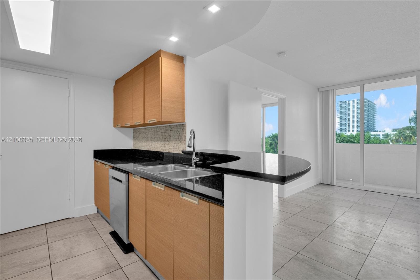 Kitchen featuring light-wood cabinetry, dark stone countertops with a breakfast bar, stainless steel dual-basin sink with a gooseneck faucet, and ceramic tile flooring