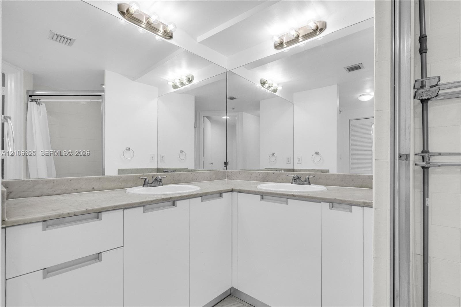 Corner vanity featuring white cabinetry, dual undermount sinks, stone countertops, and a full-width wall mirror