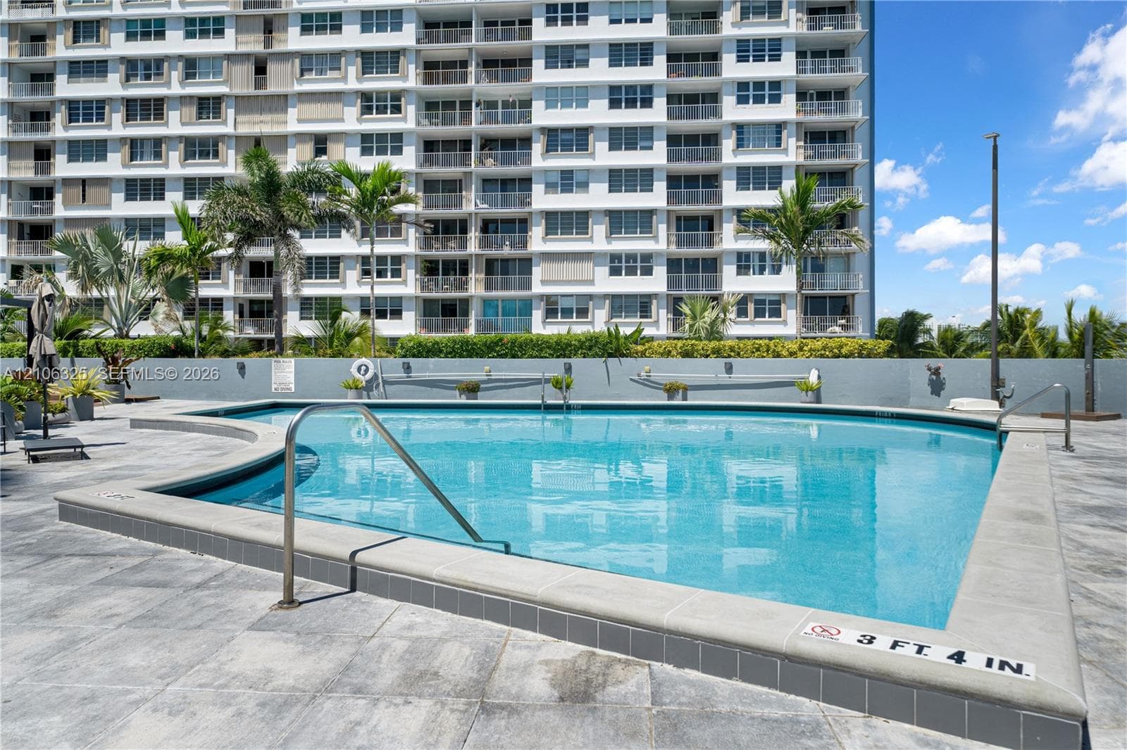 In-ground swimming pool featuring tile coping, metal handrails, a concrete paver pool deck, and landscaping