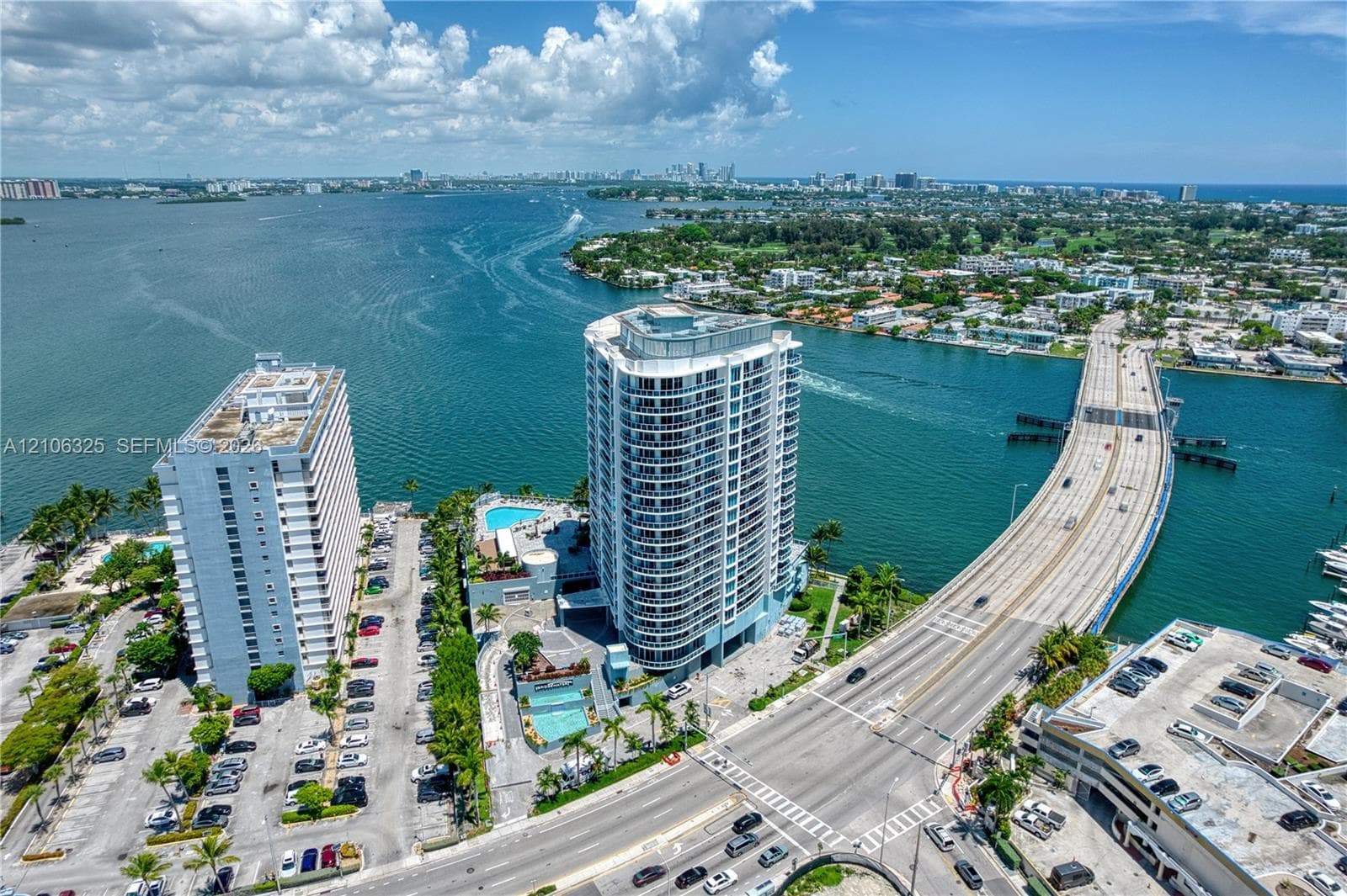 High-rise coastal property featuring waterfront positioning, an expansive pool deck, exterior balconies, and paved on-site parking