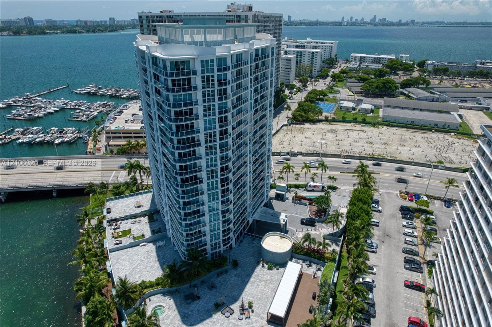 High-rise residential tower featuring a glass-paneled exterior, expansive stone-paved pool deck, elevated podium structure, and coastal orientation