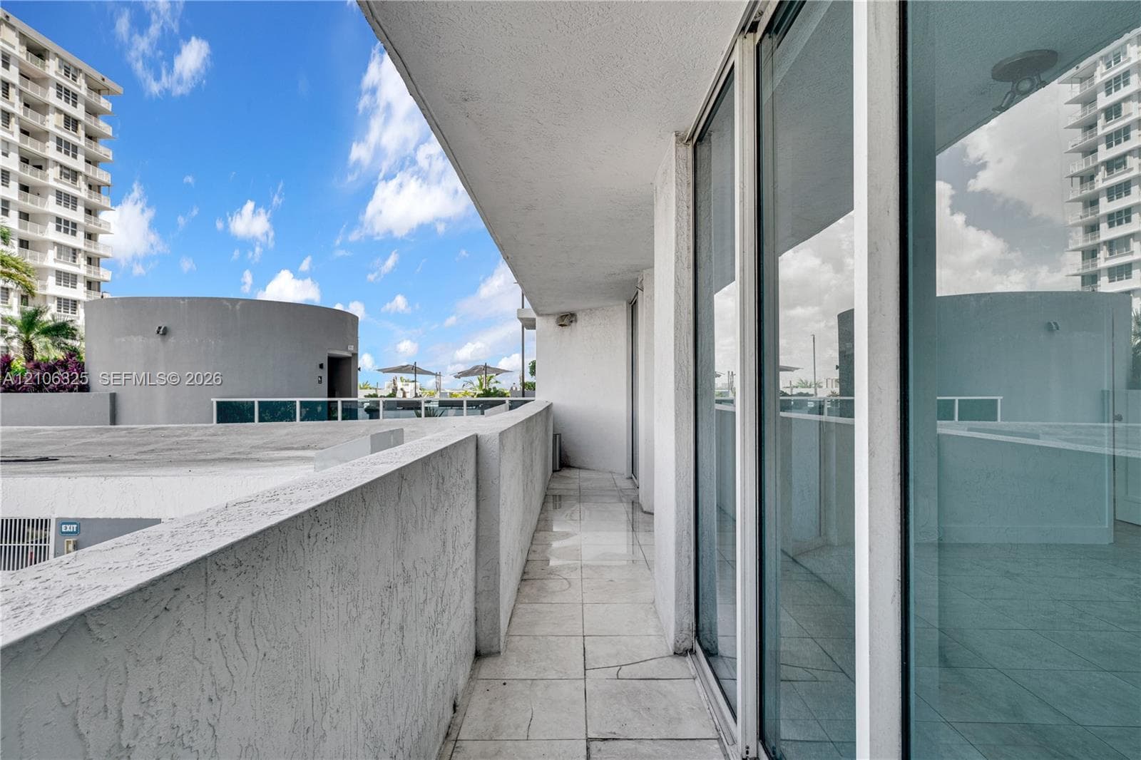 Covered balcony featuring concrete walls, tile flooring, and floor-to-ceiling glass sliding doors