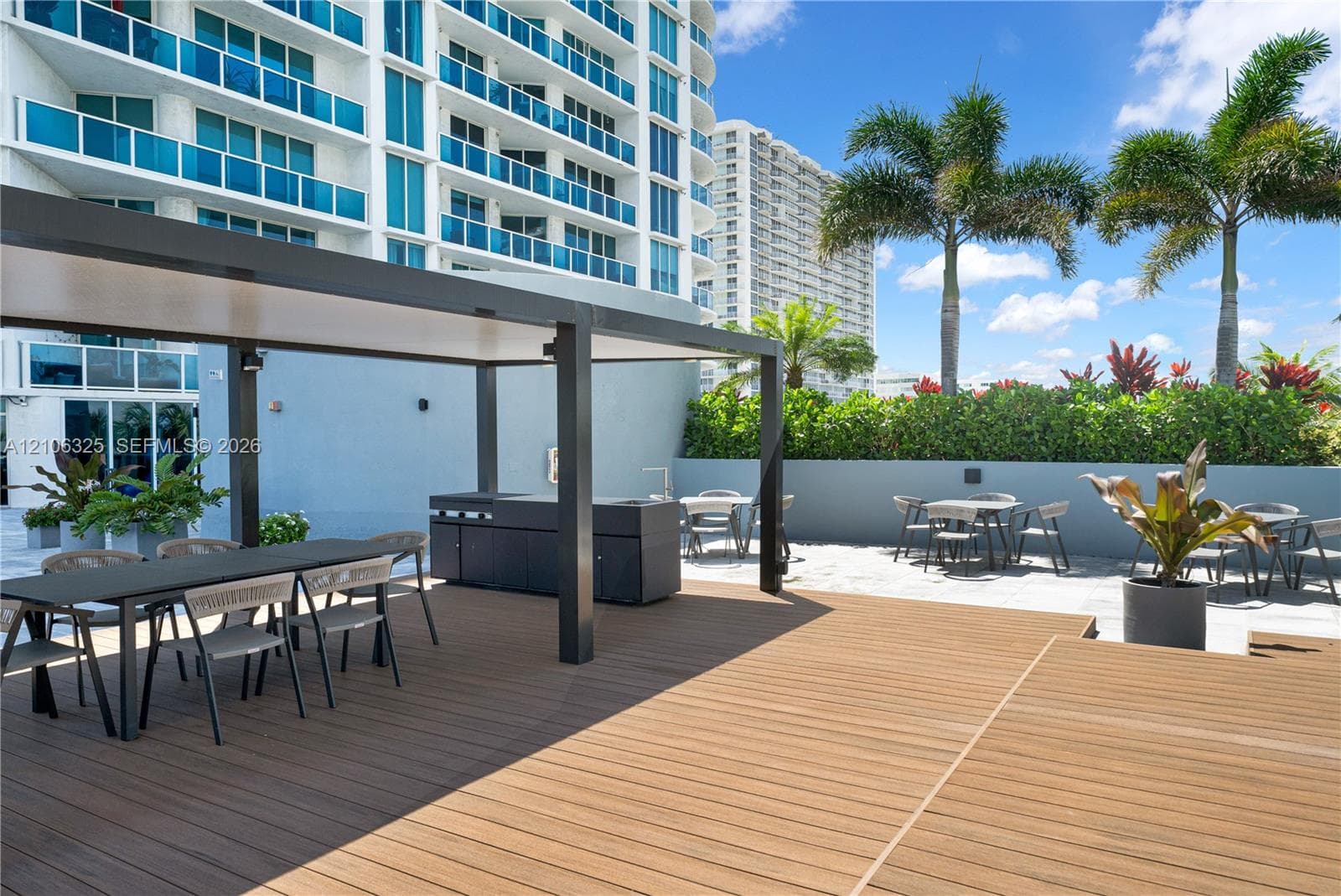 Outdoor terrace featuring a wood-finish deck, covered pergola, built-in outdoor kitchen with a stainless steel grill, and masonry perimeter wall