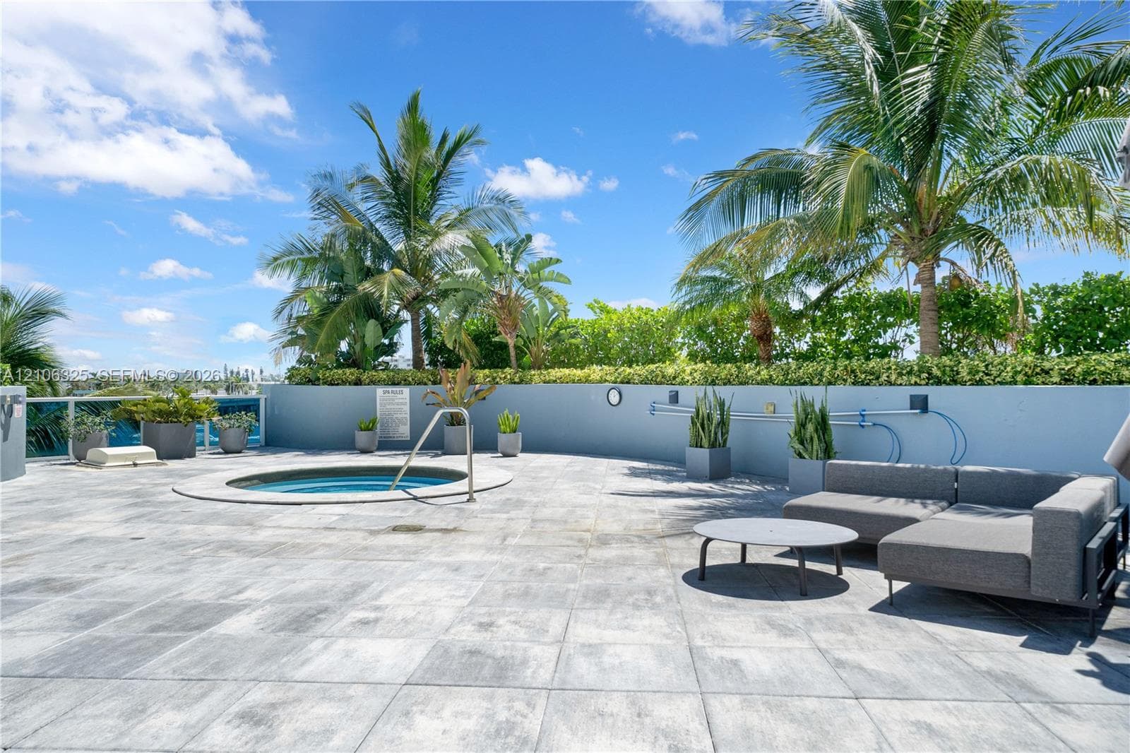 Rooftop terrace featuring large-format tile flooring, a built-in spa, perimeter privacy wall, and mature landscaping