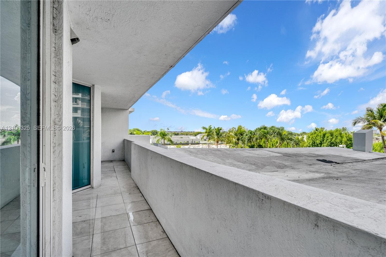 Covered balcony featuring concrete flooring, a solid half-wall railing, and large-panel sliding glass doors