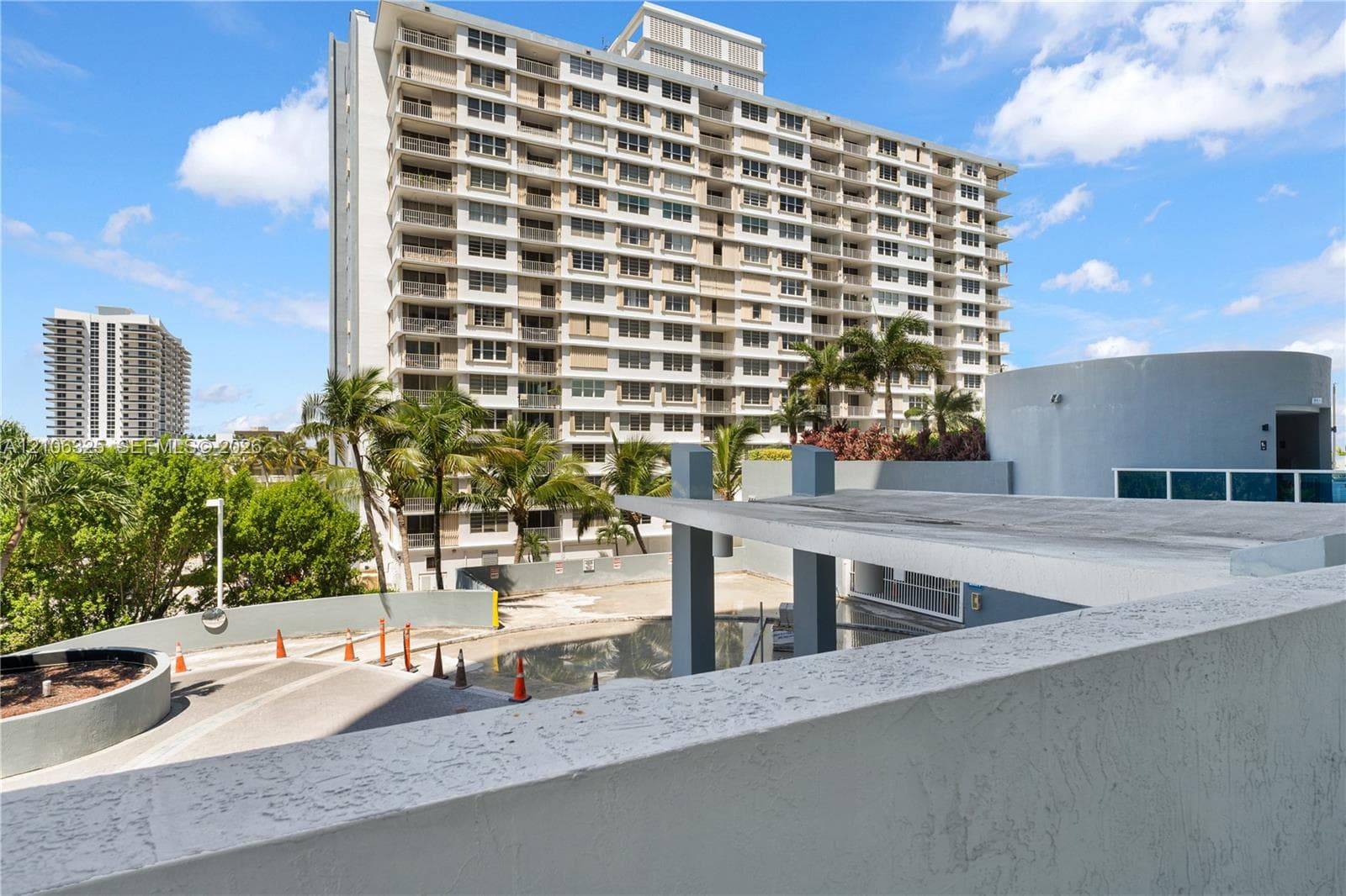 High-rise condominium building featuring private balconies, concrete construction, paved motor court, and mature tropical landscaping