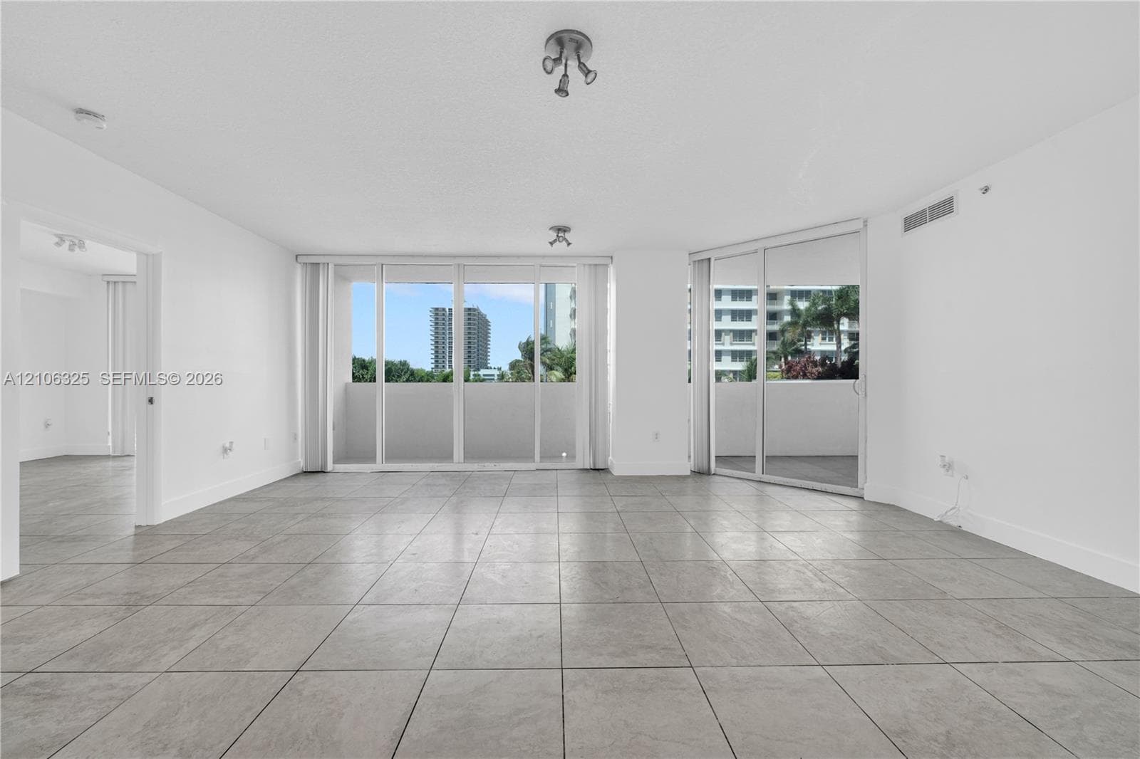 Open interior space featuring large-format stone-style tile flooring, floor-to-ceiling glass sliding doors, and dual access to an expansive balcony