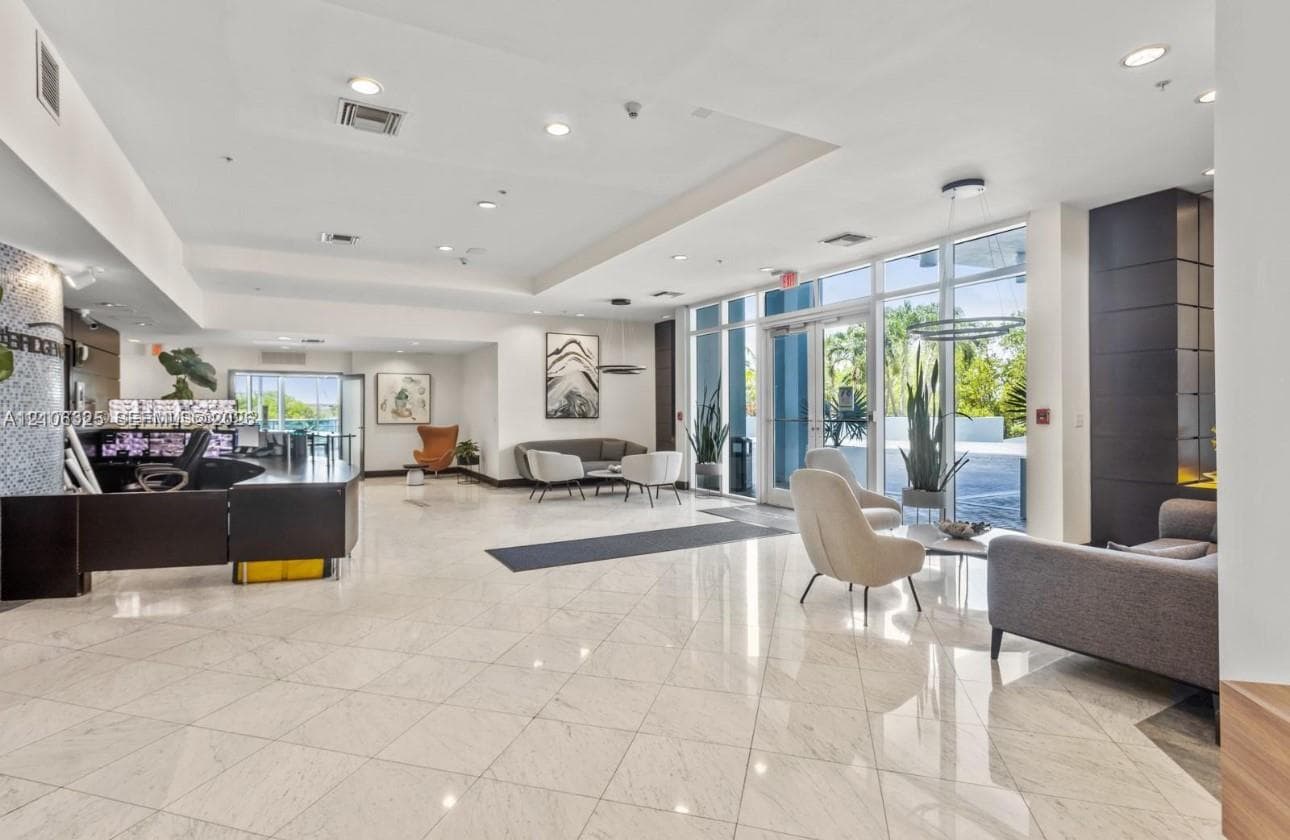 Expansive lobby featuring polished stone flooring, floor-to-ceiling windows, built-in reception desk, recessed lighting, and contemporary architectural detailing