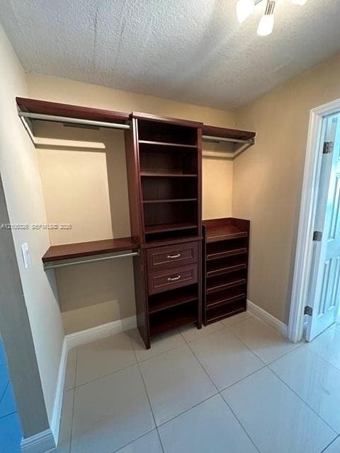 Walk-in closet featuring custom built-in dark wood cabinetry, two storage drawers, integrated shelving, tiered shoe storage, and ceramic tile flooring
