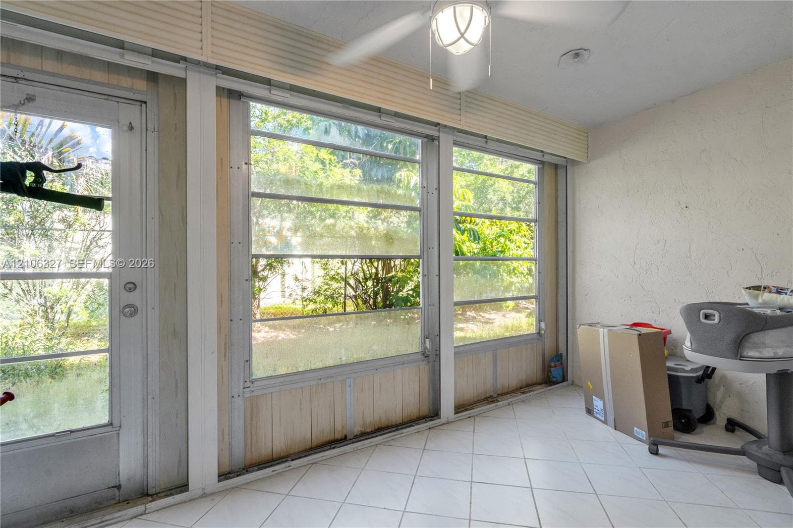 Enclosed sunroom featuring white tile flooring, floor-to-ceiling multi-pane windows, a central ceiling fan with an integrated light fixture, and a glass-paneled exterior door