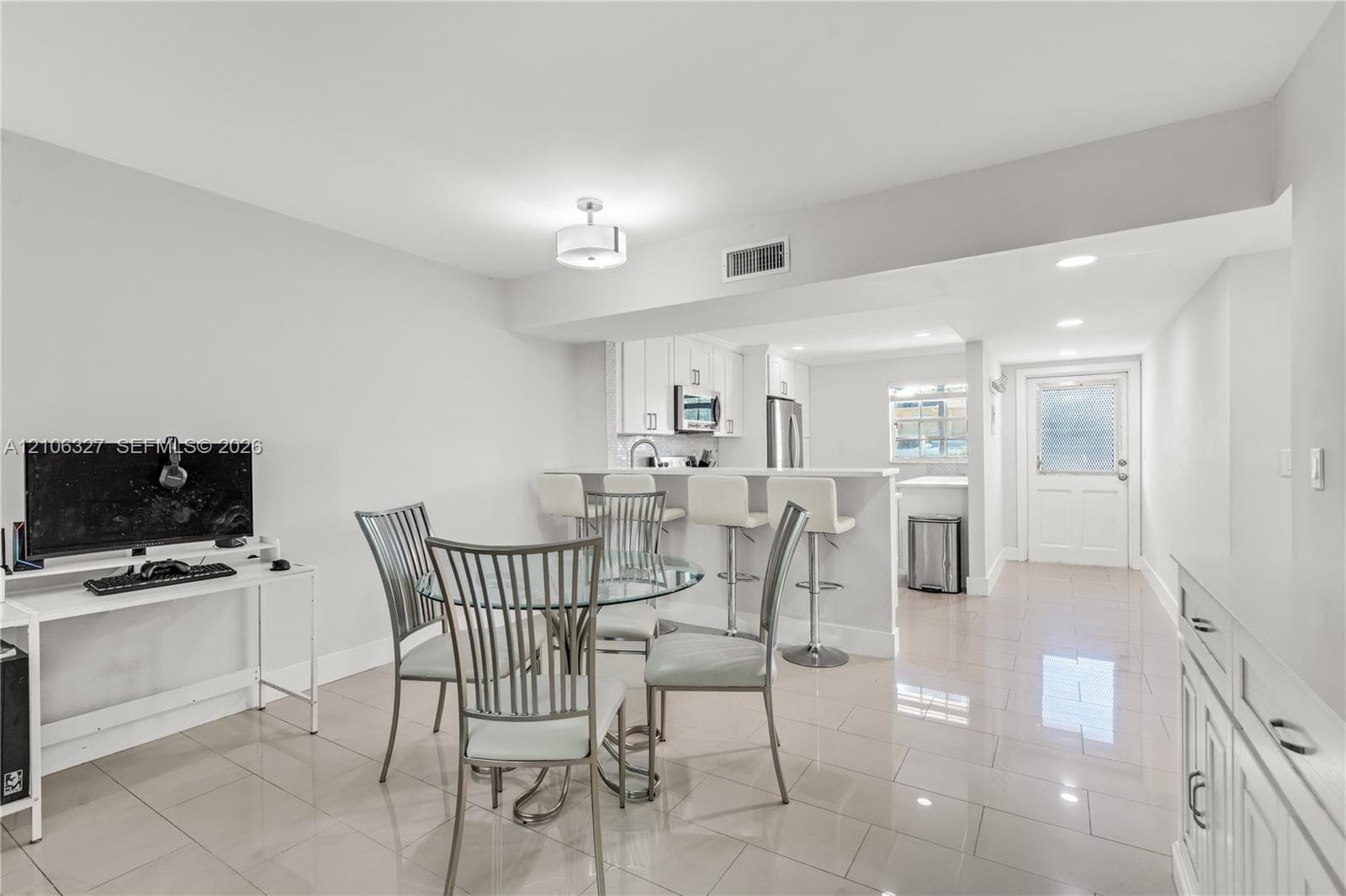 Open-concept interior featuring light-toned tile flooring, white cabinetry with integrated kitchen appliances, a breakfast bar, recessed lighting, and a neutral color palette