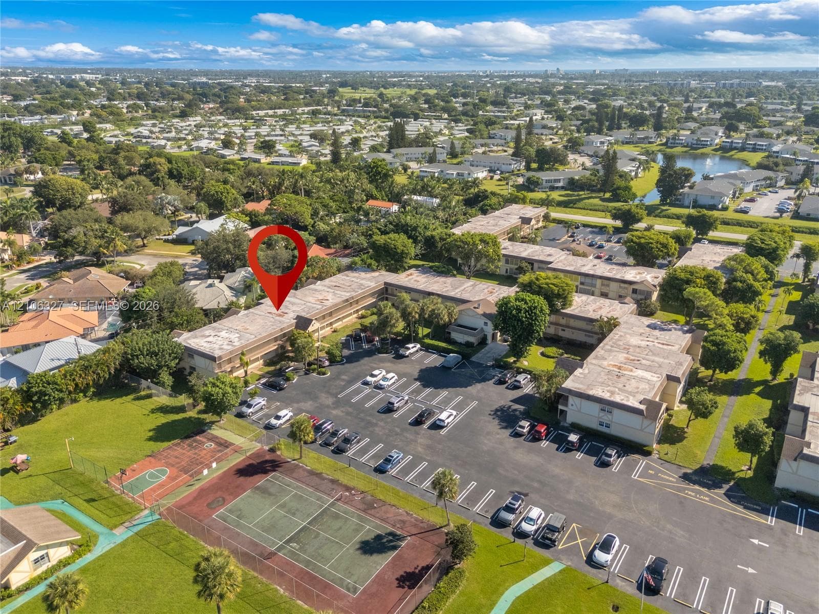 Aerial perspective of a multi-story residential complex featuring dedicated surface parking, on-site tennis courts, and landscaped green space