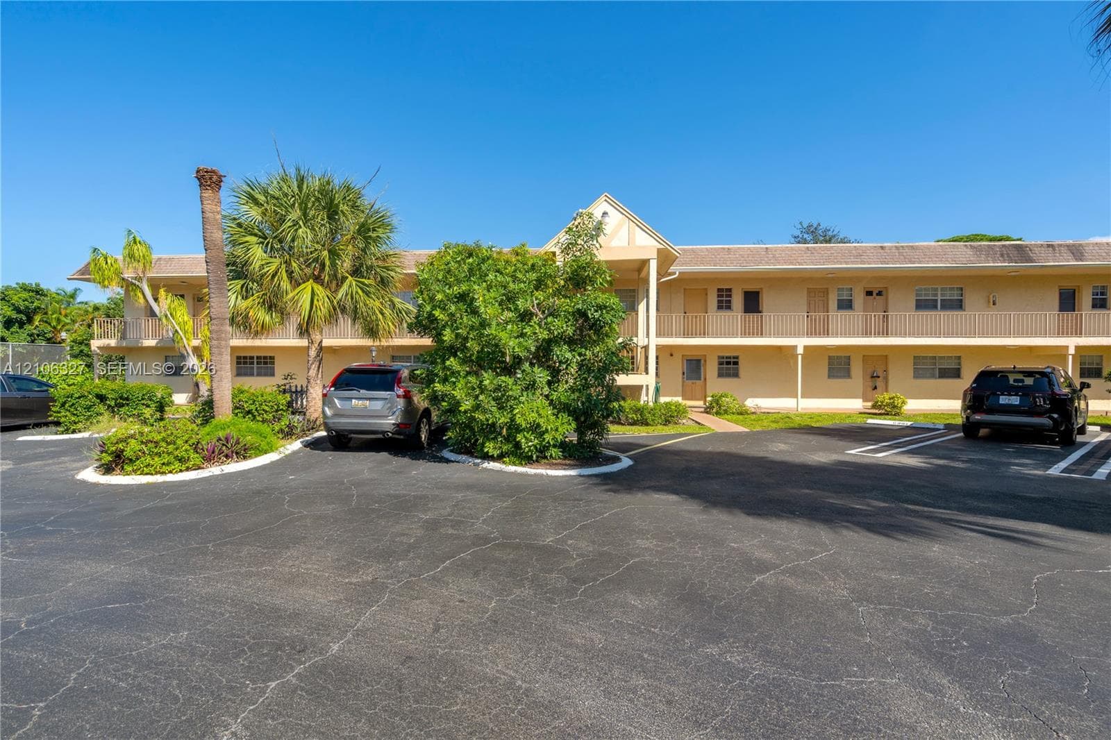 Two-story exterior featuring a gabled roofline, stucco facade, second-level railed balcony, and on-site asphalt parking