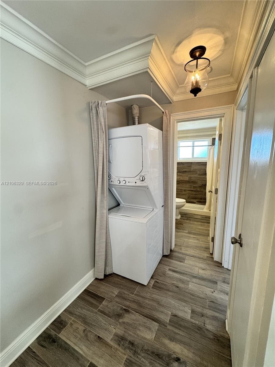 Laundry area featuring stacked laundry appliances, recessed ceiling crown molding, wood-finish flooring, and a decorative pendant light fixture