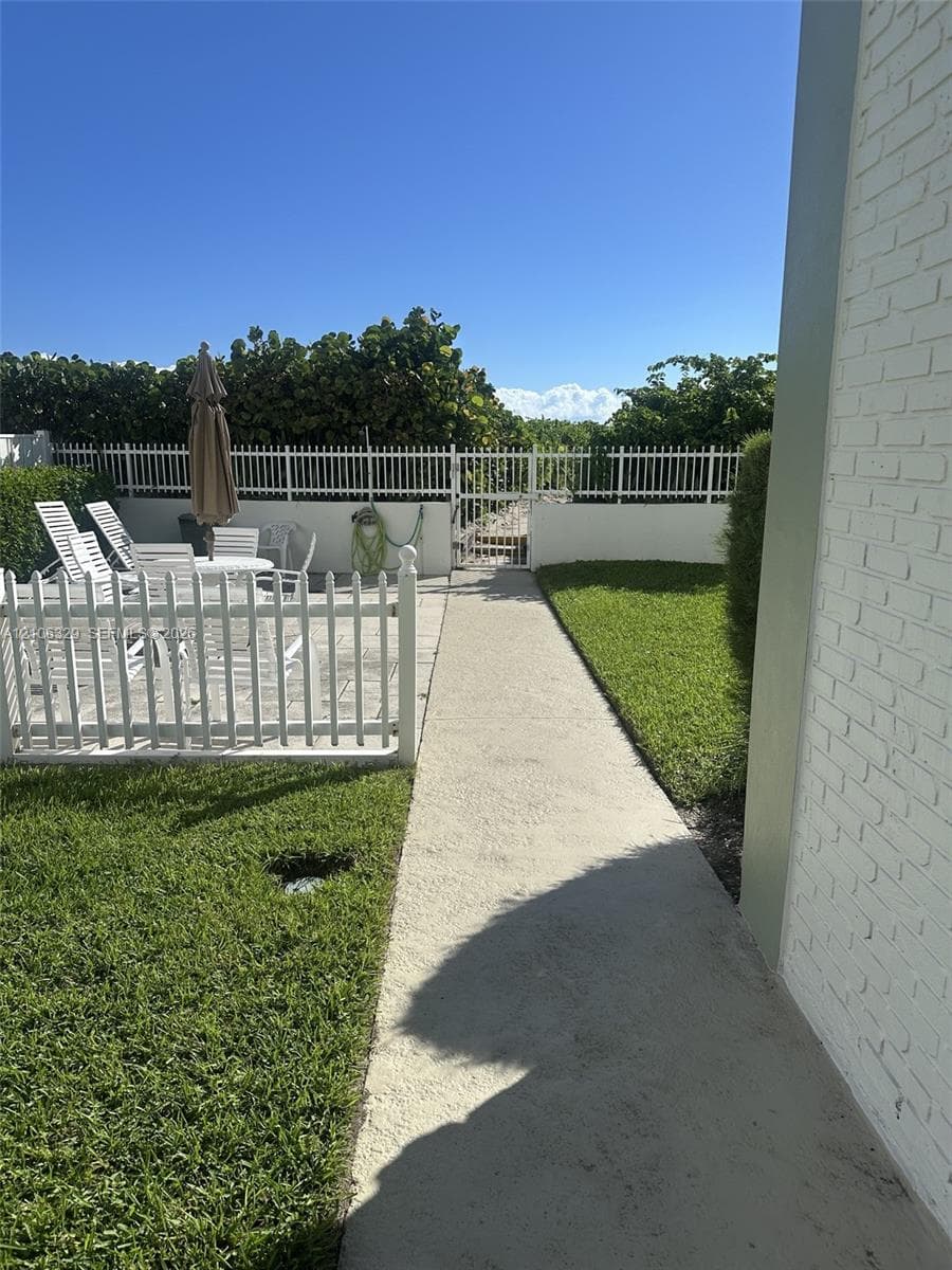 Backyard featuring a paved patio, white vinyl fencing, a concrete walkway, and a manicured lawn