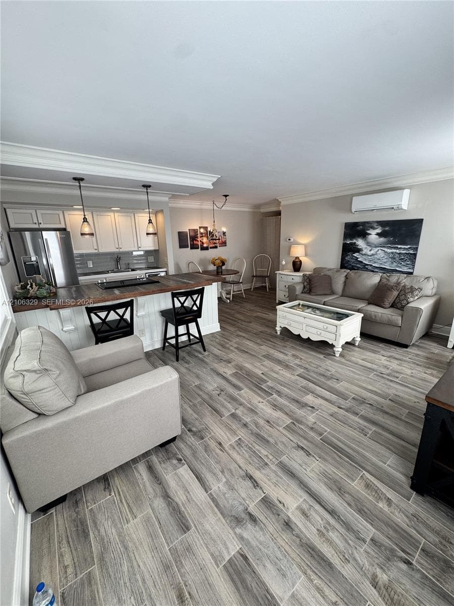 Open-concept area featuring wood-finish tile flooring, white cabinetry with crown molding, a breakfast bar with a wood countertop, and dual pendant lighting