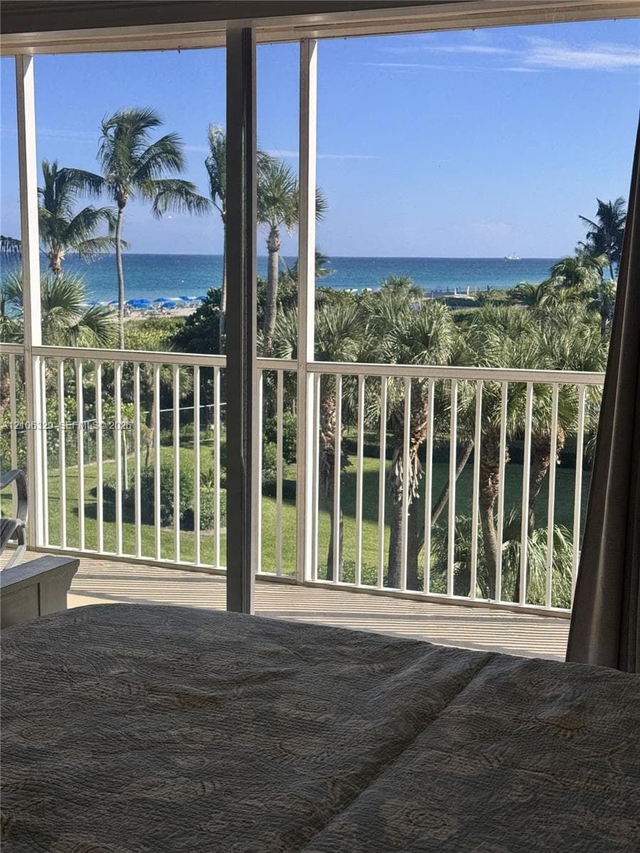 Screened balcony featuring vertical white railing and coastal scenery including palm trees and ocean