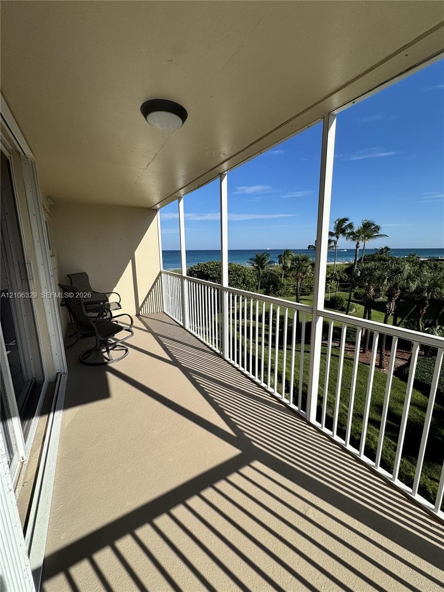 Covered balcony with white metal railings, concrete flooring, and ceiling-mounted light fixture
