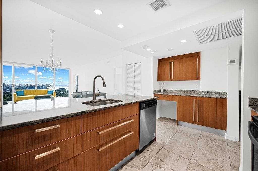 Kitchen featuring wood-finish cabinetry with linear pulls, stone-surfaced countertops, a stainless steel undermount sink with a gooseneck faucet, stainless steel dishwasher, and tile flooring