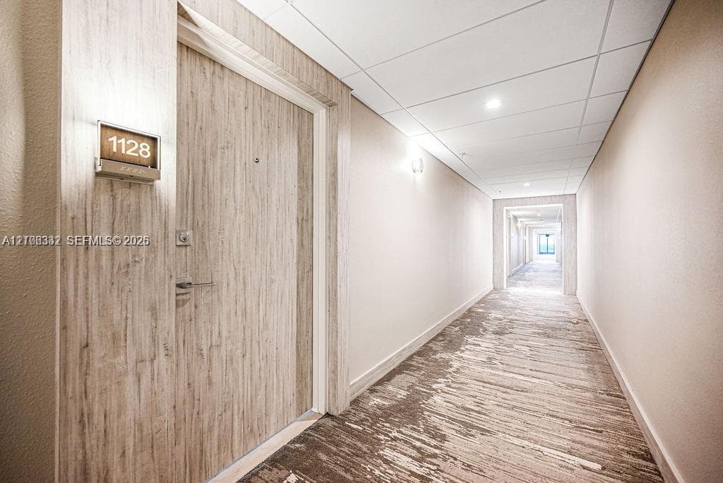 Wood-finish door with brushed metal hardware, recessed ceiling lighting, and wall-mounted unit signage