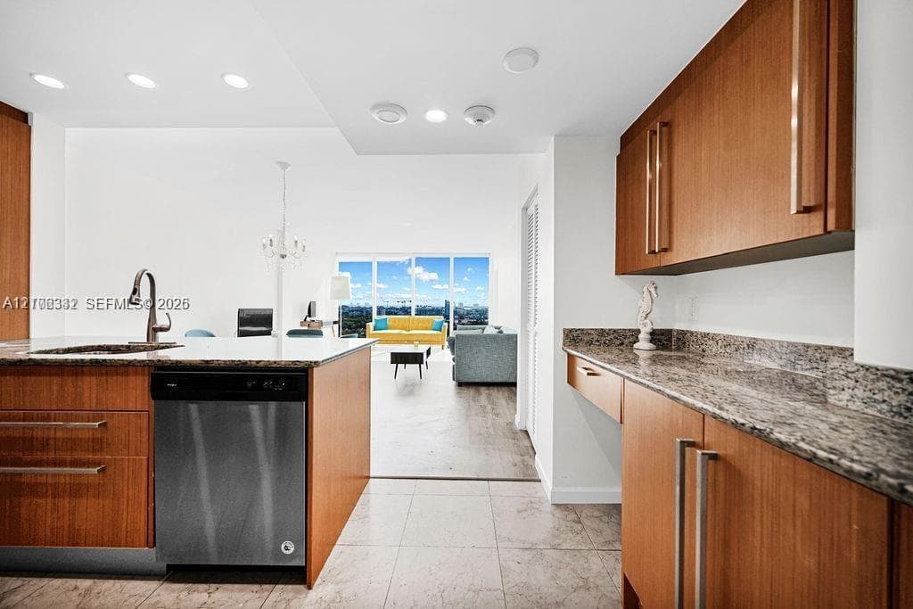Kitchen featuring flat-panel wood-finish cabinetry, stone countertops, stainless steel dishwasher, undermount sink with arched faucet, and recessed lighting
