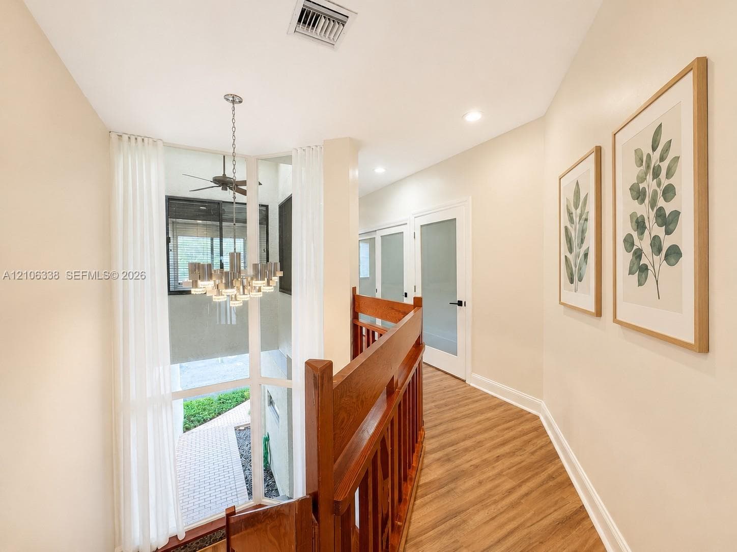 Floor-to-ceiling windows, wood-finish flooring, multi-tiered metal chandelier, wooden stair railing, and frosted glass panel interior doors
