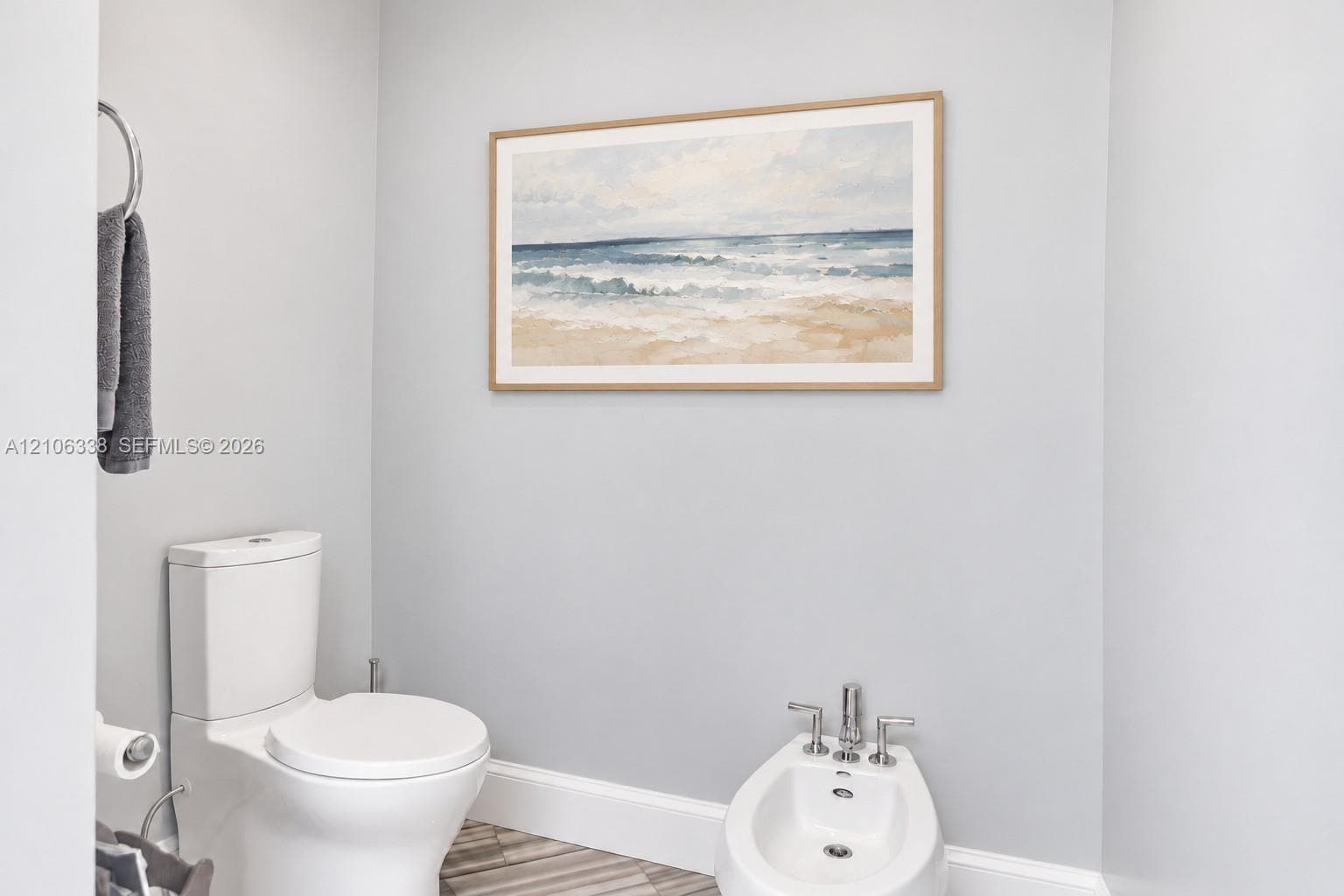 White porcelain toilet, bidet with chrome hardware, and metallic circular towel ring