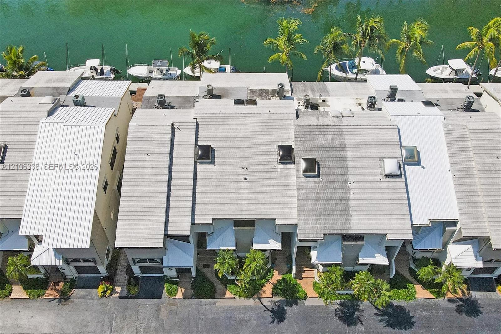 Aerial perspective of waterfront property featuring multiple skylights, shingle roofing, and established palm trees along the bulkhead