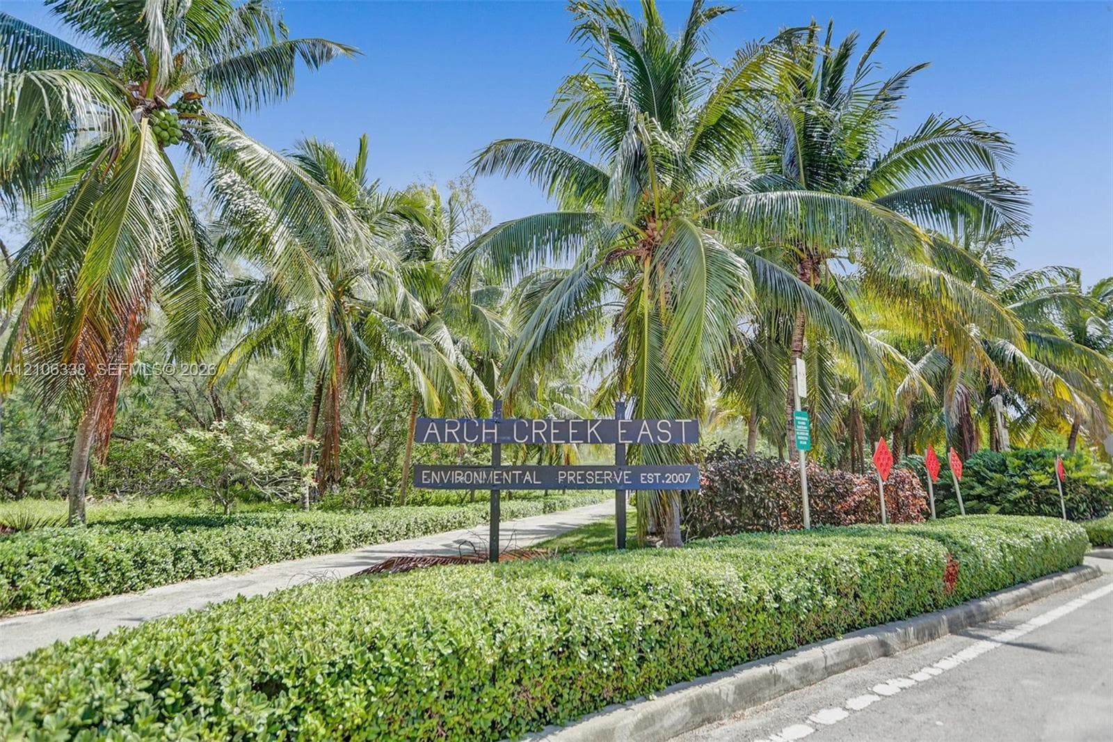Arch Creek East Environmental Preserve entrance featuring mature palm trees, manicured hedges, and paved pathways