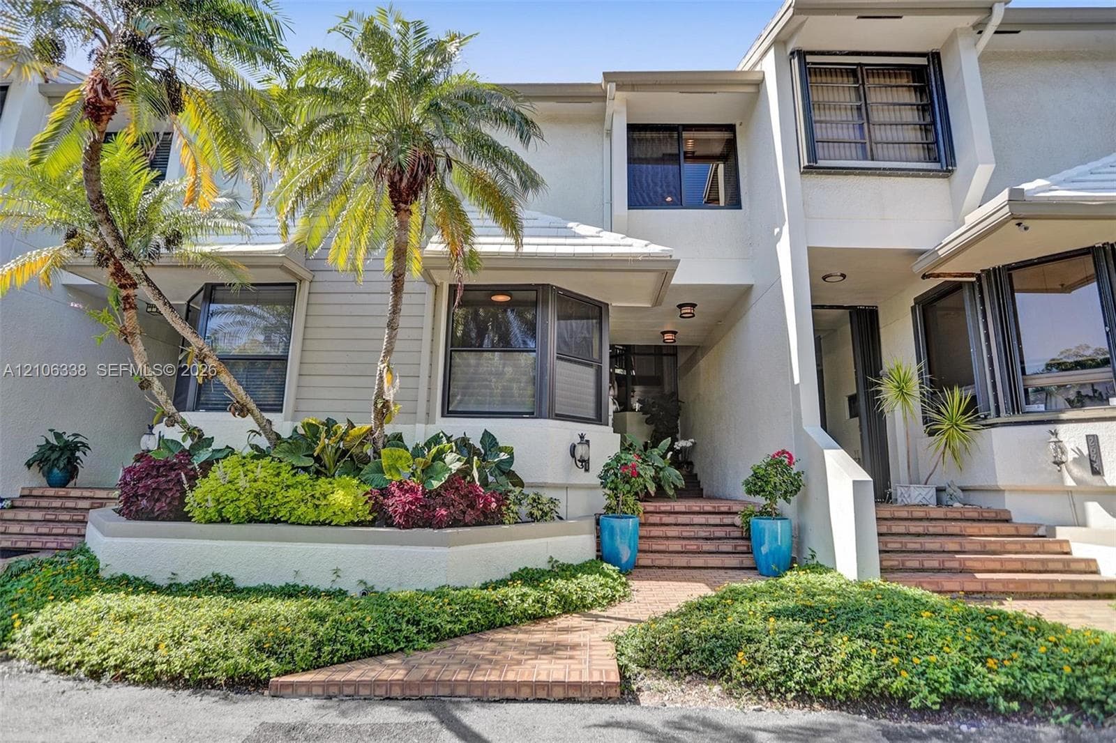 Multi-level exterior featuring stucco siding, bay windows, integrated brick pathways, terraced landscaping, and a tiered staircase entrance