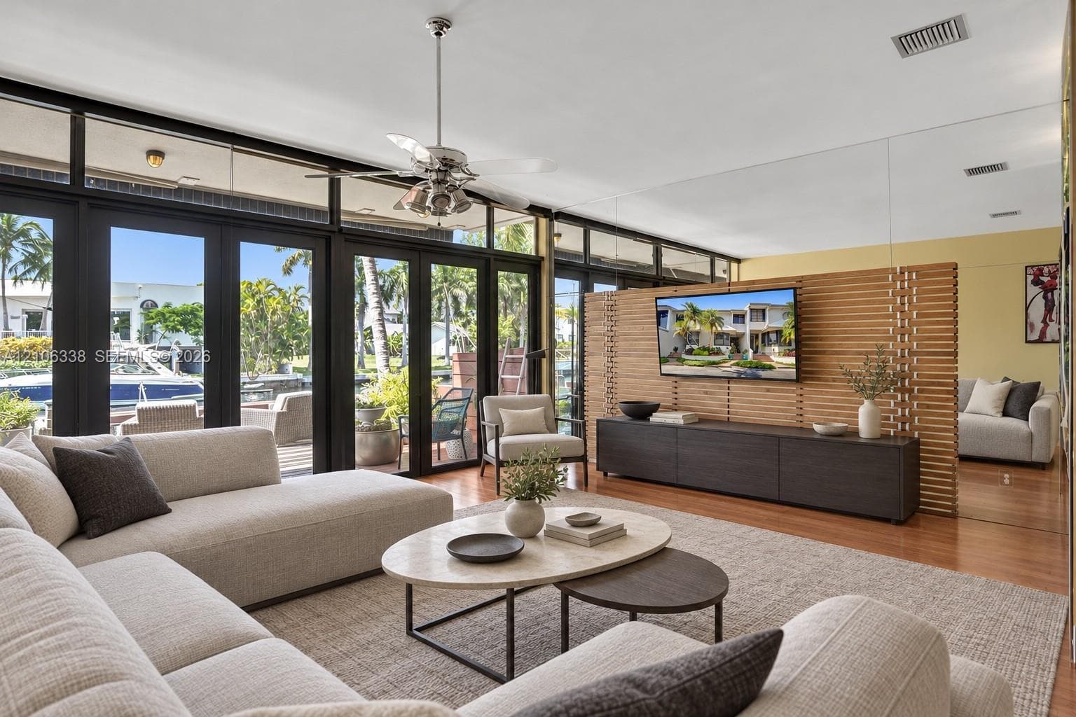 Floor-to-ceiling glass paneling with dark-framed exterior doors, horizontal wood-slat room divider, mirror-paneled wall, and wood-finish flooring