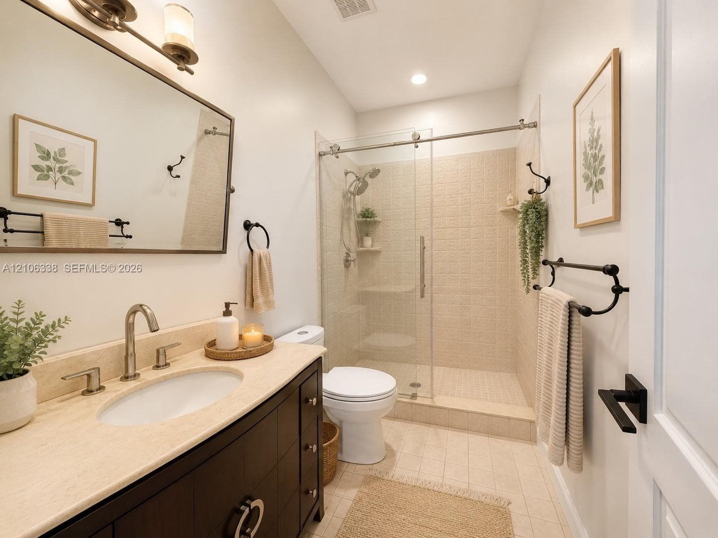 Bathroom featuring a dark-finish vanity with a neutral stone countertop, undermount sink, walk-in shower with sliding glass doors, and matte black hardware