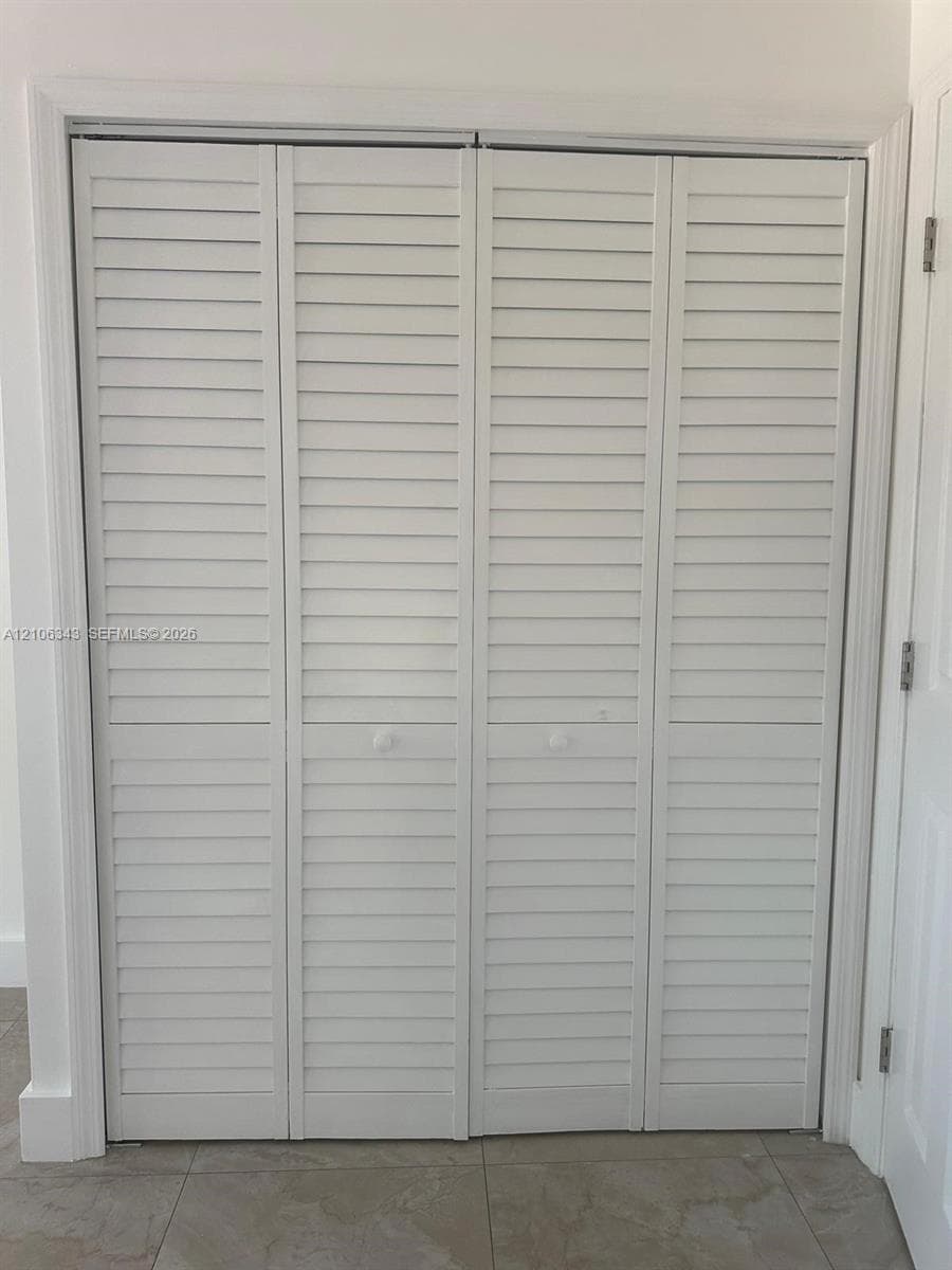 White four-panel bifold closet door featuring louvered slats and central round knobs