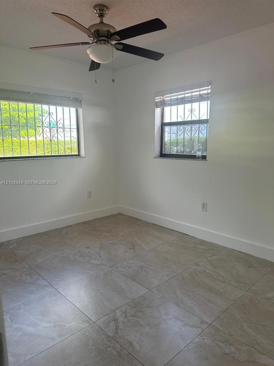 Neutral-toned tile flooring, ceiling fan with integrated lighting, and metal security bars on exterior windows