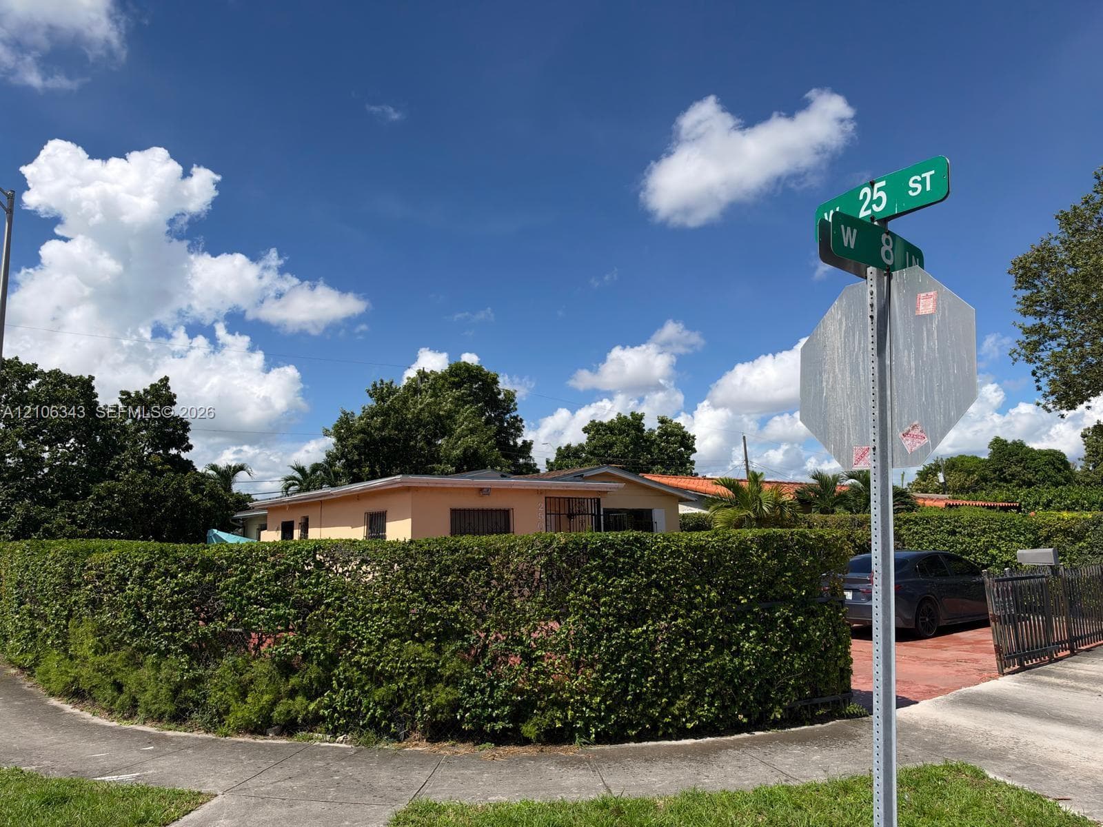 Single-story residence featuring stucco exterior, flat roof, and perimeter privacy hedging