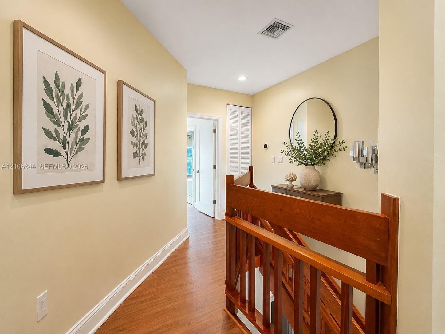 Hallway featuring wood-finish flooring, a wood balustrade staircase railing, and a circular wall-mounted mirror