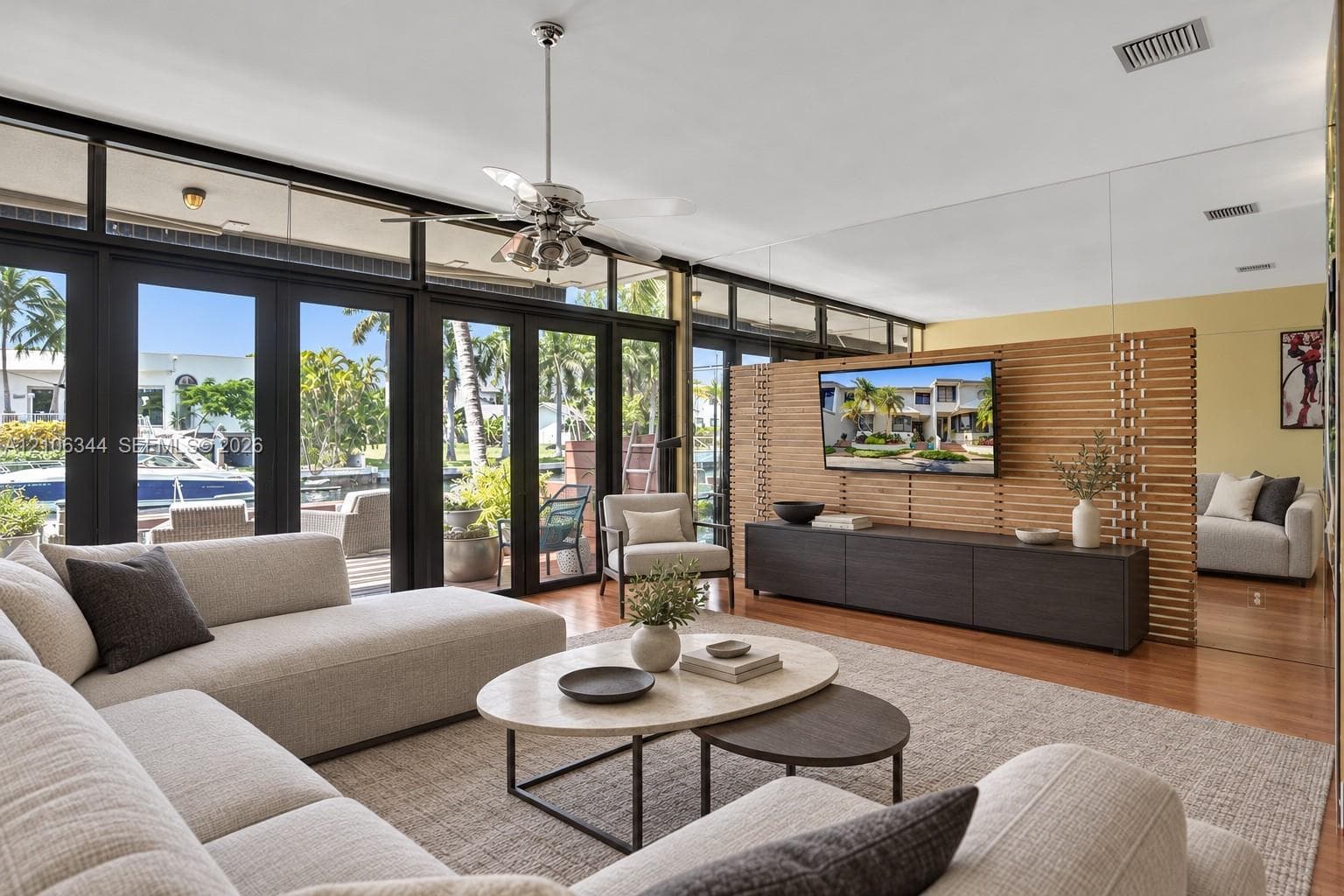 Floor-to-ceiling glass paneling with dark-framed exterior doors, horizontal wood-slat room divider, mirror-paneled wall, and wood-finish flooring